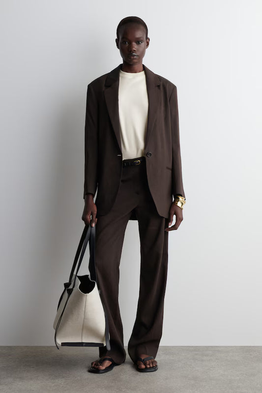 Man wearing a brown suit holding a white bag against a plain background