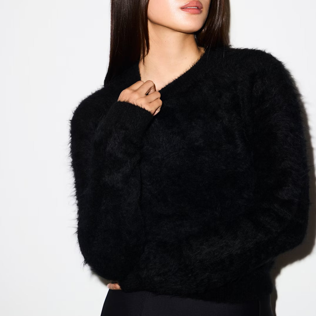 Black fuzzy sweater worn by a person on a white background