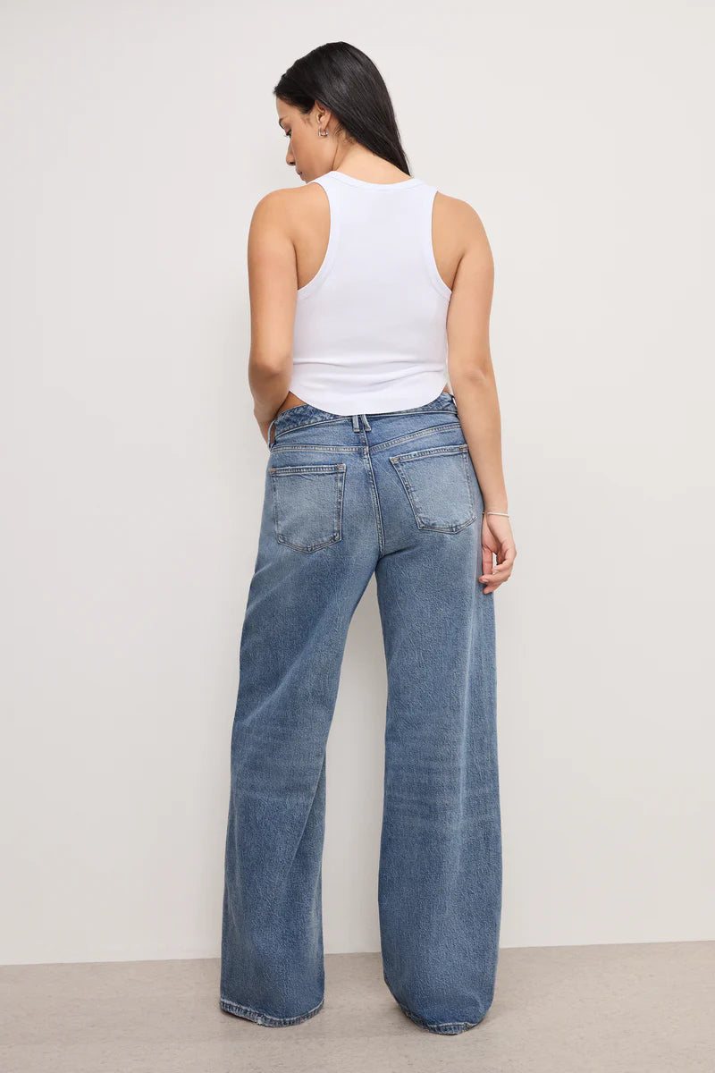 Woman wearing a white tank top and blue jeans against a plain background