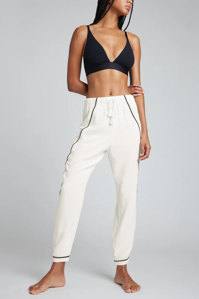Person wearing a black bra and white pants with black piping on a gray background