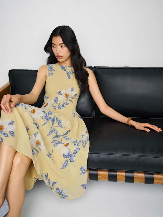 Woman in a yellow floral dress sitting on a black leather couch against a white background