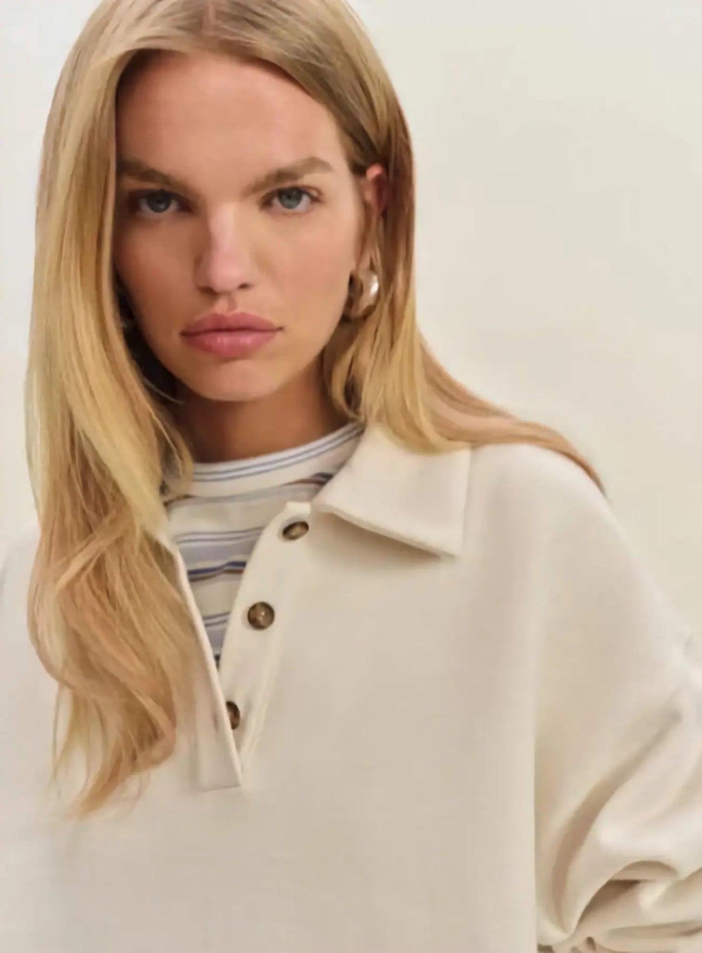 Woman in a modern setting wearing the Nico Classic Polo Sweatshirt in cream, embodying elevated comfort and strategic recalibration.