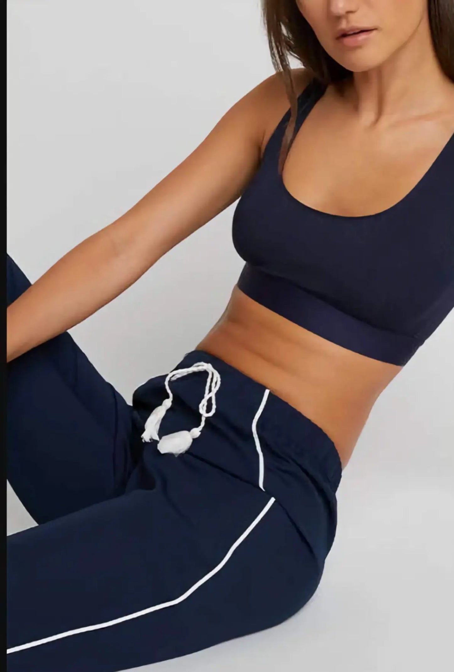 Person wearing navy sports bra and pants with white drawstrings on a light gray background