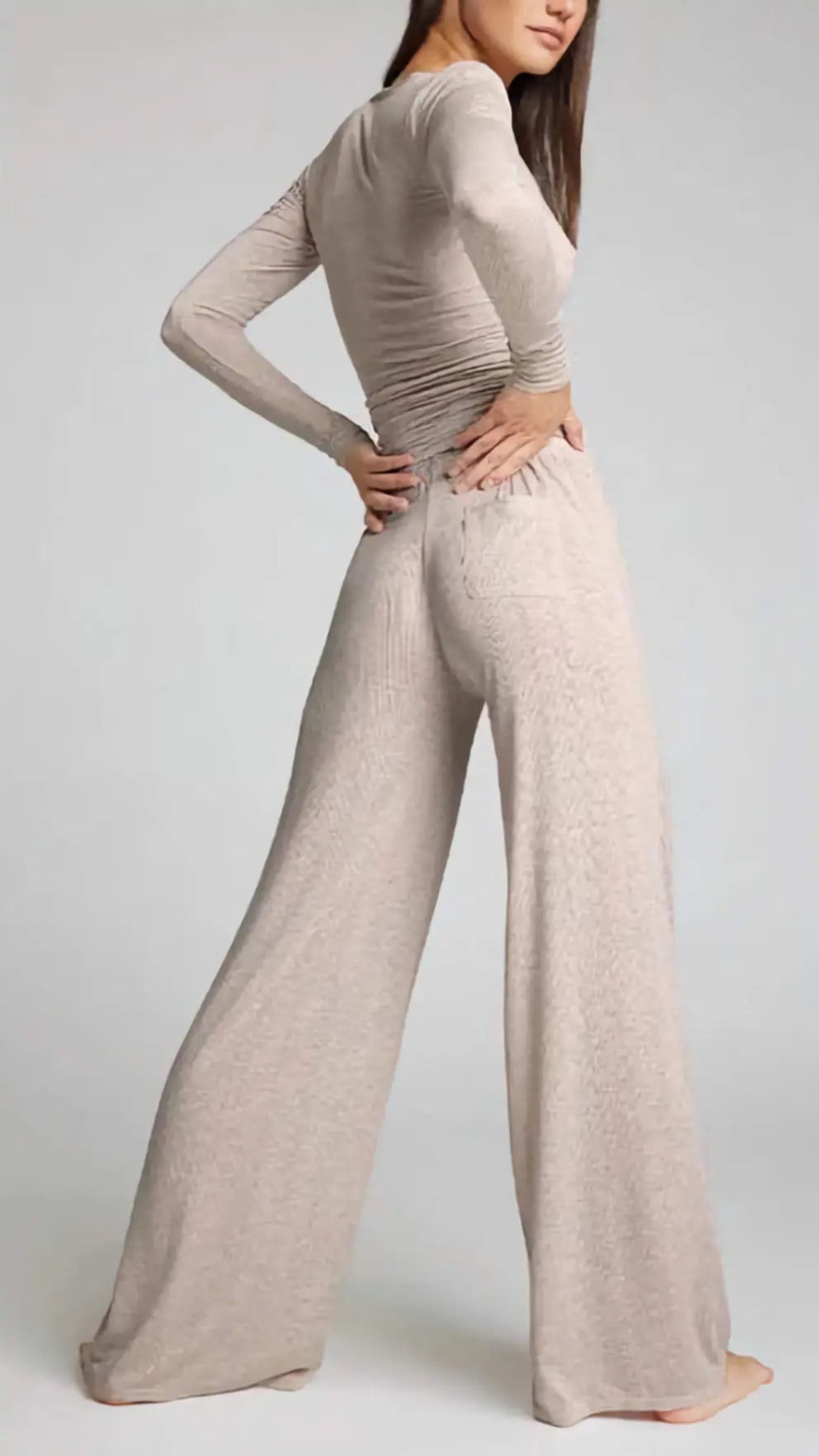 Person wearing a beige long-sleeve top and wide-leg pants on a light gray background