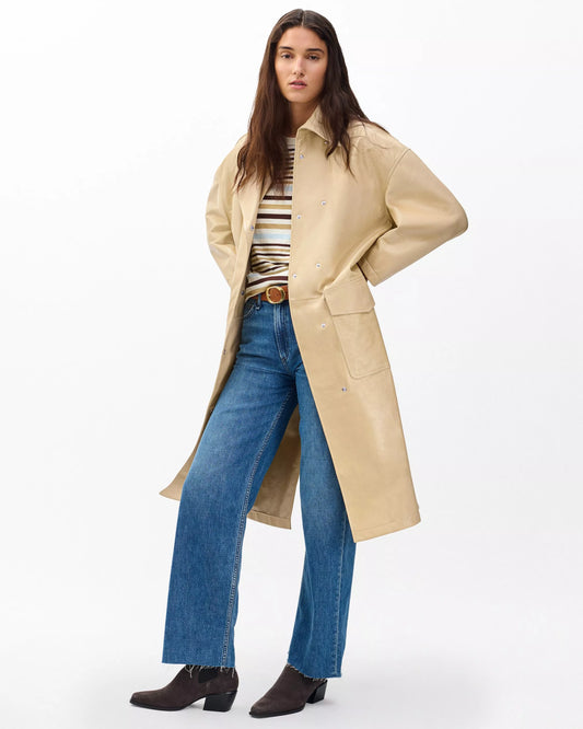 Woman wearing a beige trench coat, striped shirt, and blue jeans on a white background