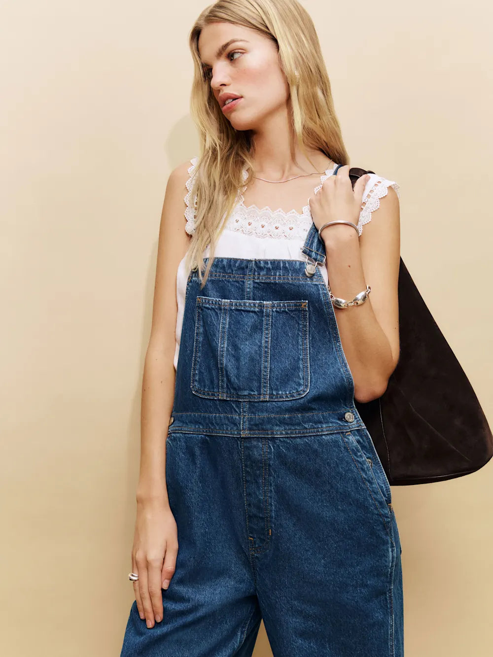 Woman wearing denim overalls against a beige background