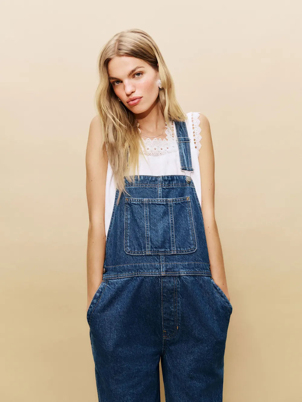 Woman wearing blue denim overalls against a beige background