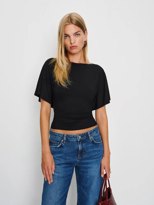 Woman wearing a black top and blue jeans against a plain background