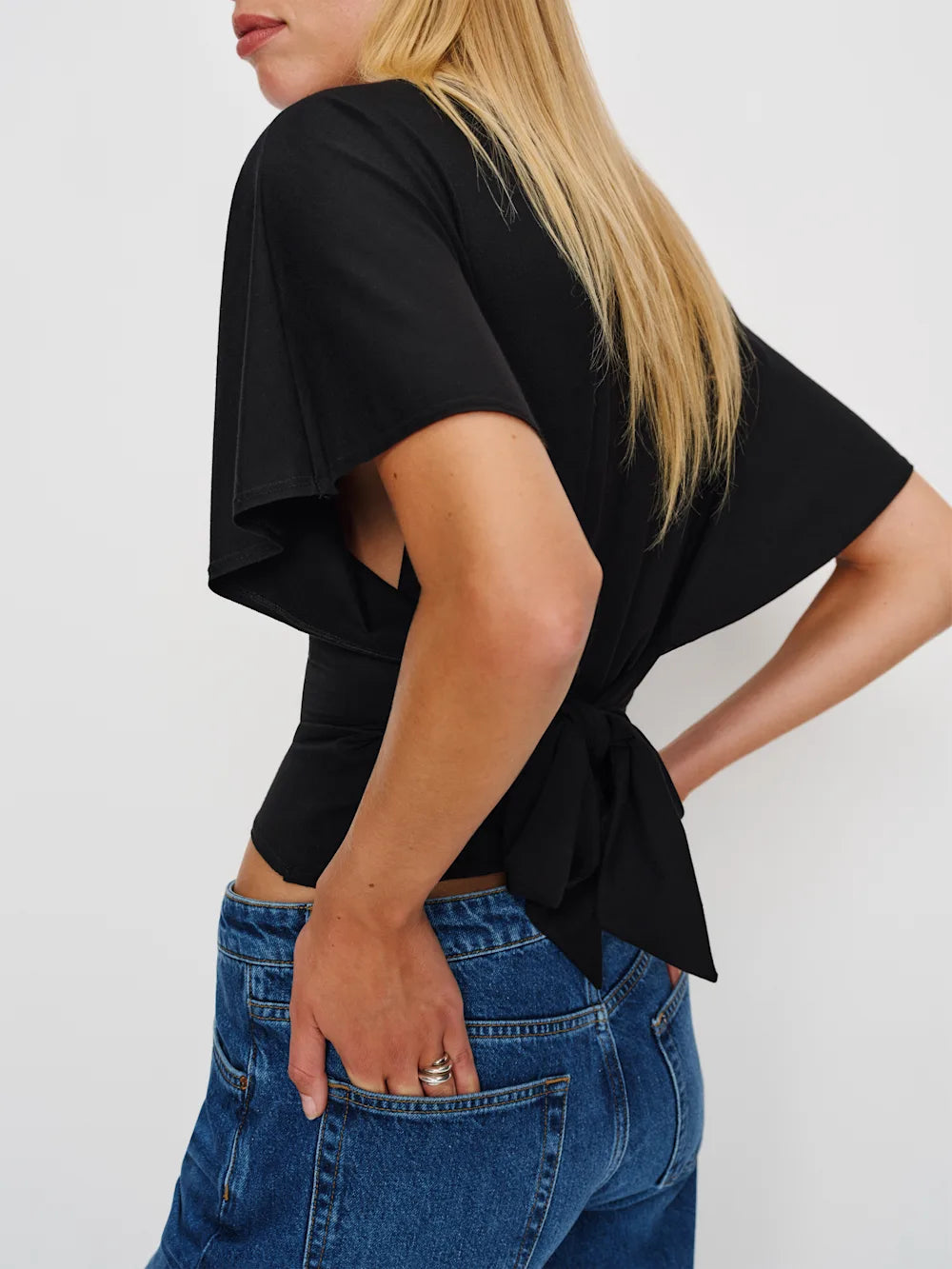 Person wearing a black top with a tie detail and blue jeans on a white background