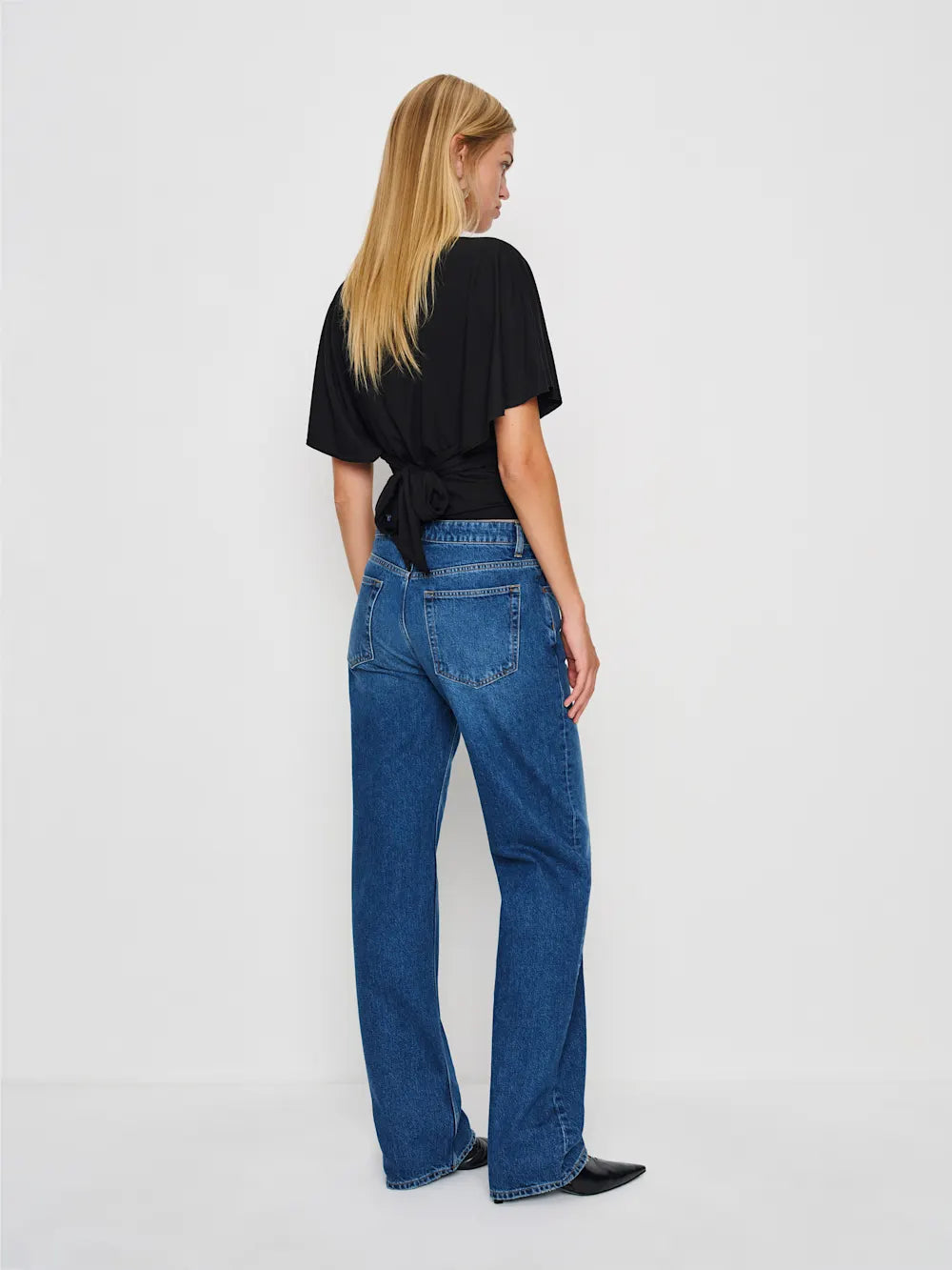 Person wearing blue jeans and a black top on a white background