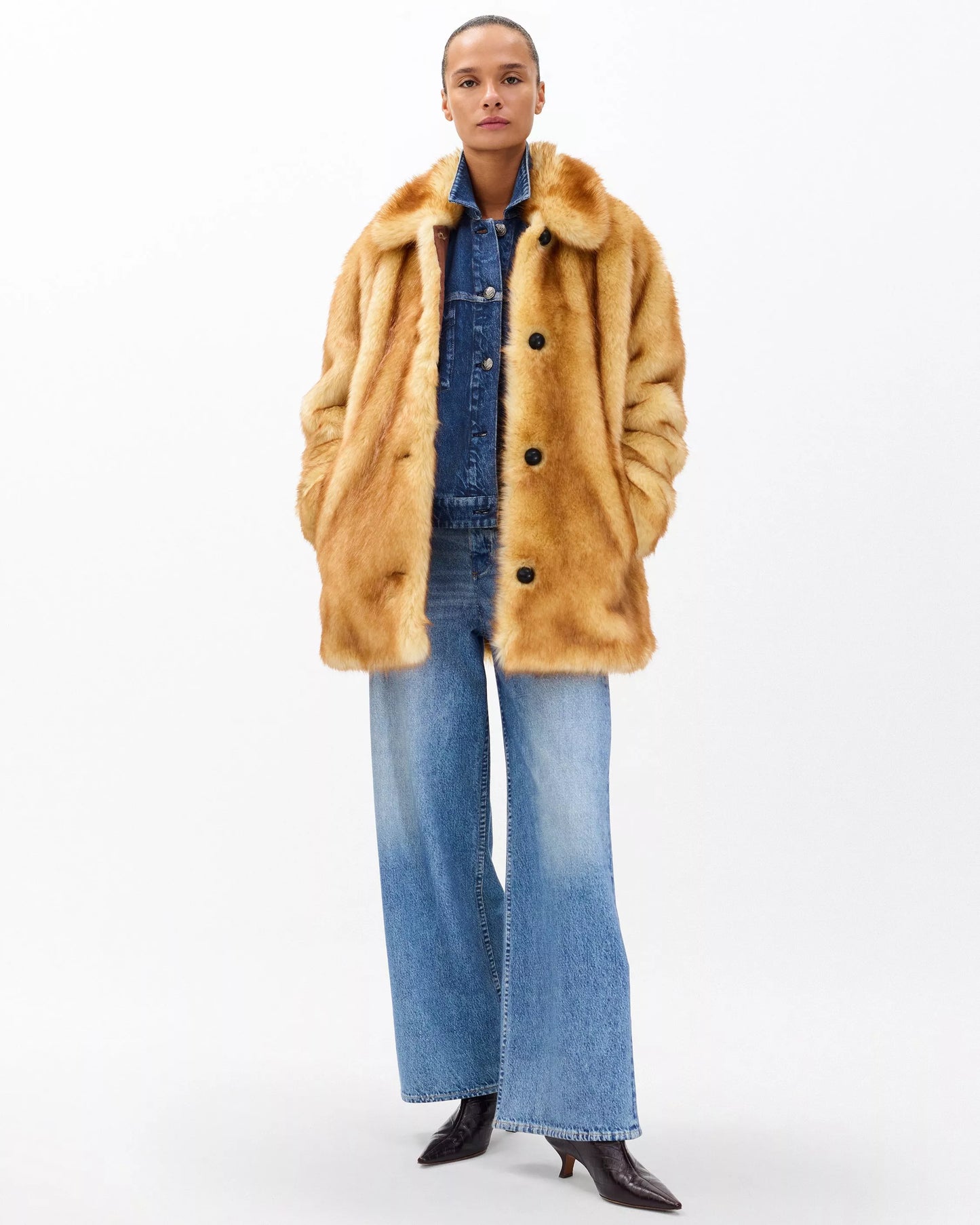 Person wearing a brown fur coat over a denim outfit on a white background