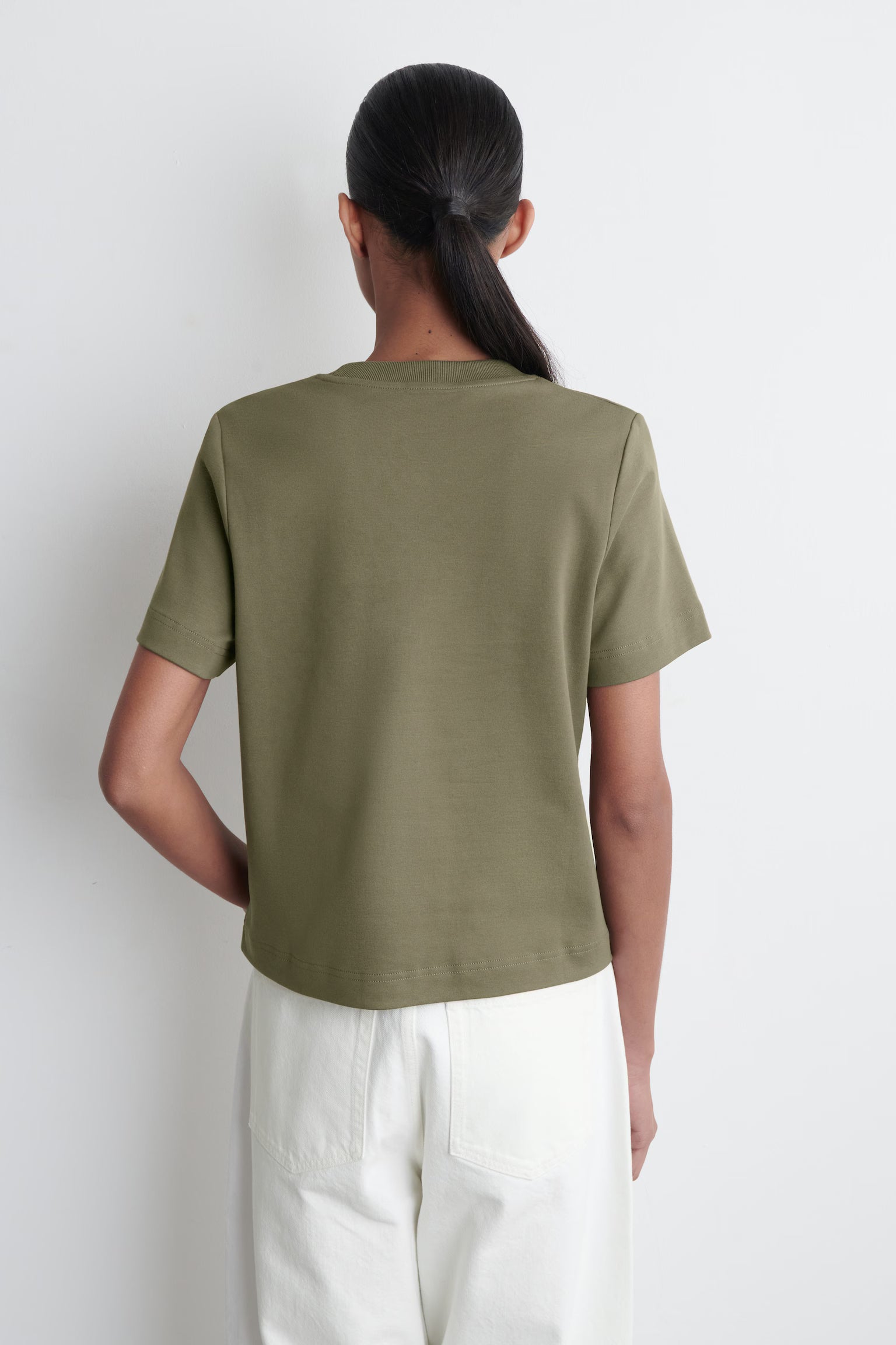 Person wearing a green t-shirt and white pants against a white background