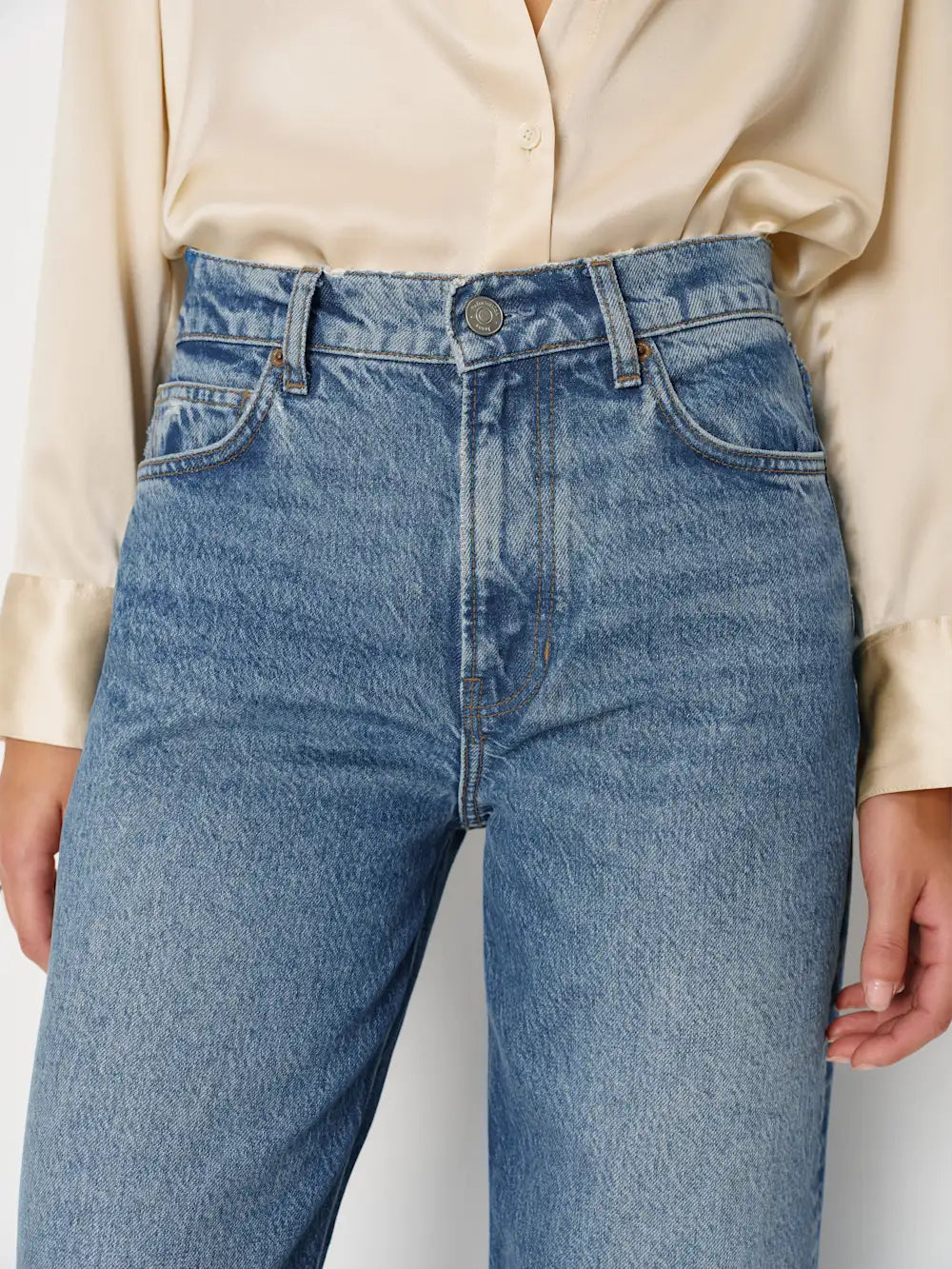 Blue jeans worn with a beige shirt on a neutral background