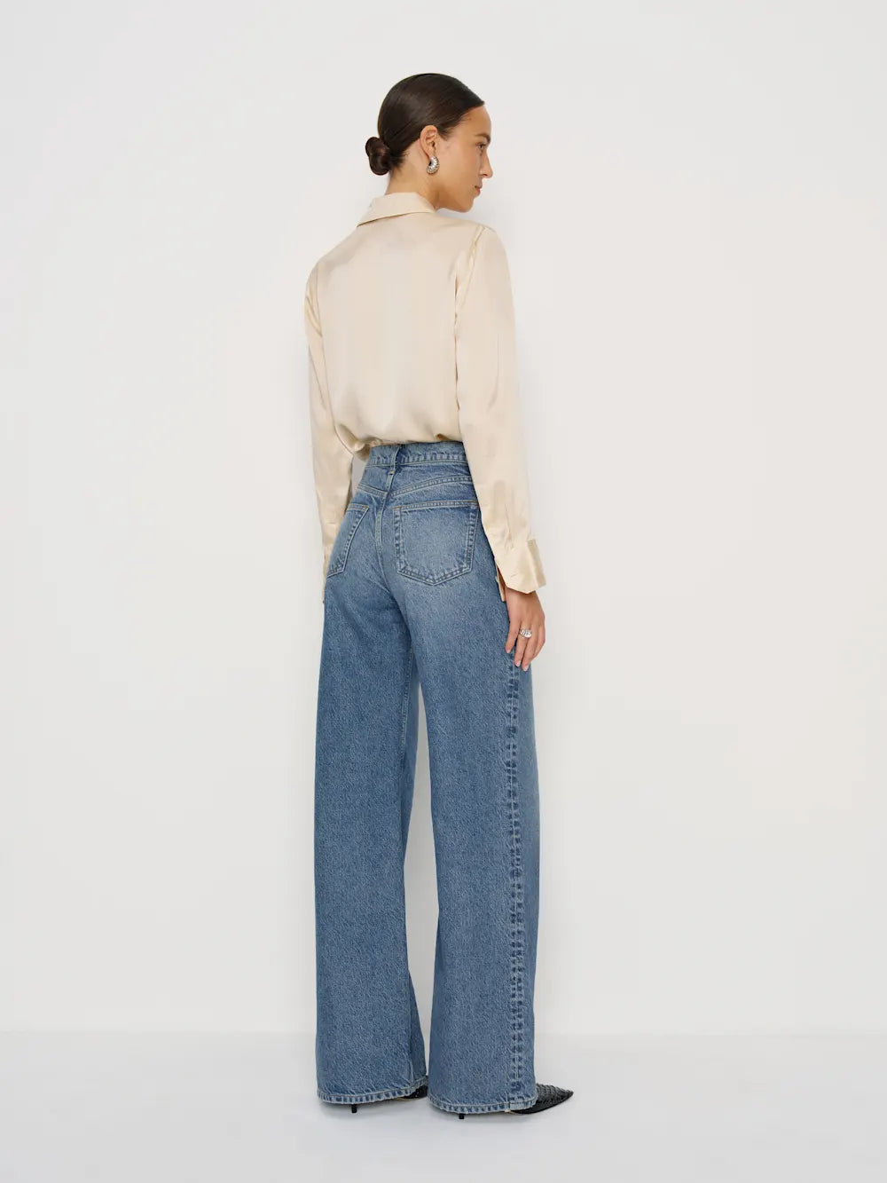 Person wearing a beige shirt and blue jeans on a white background