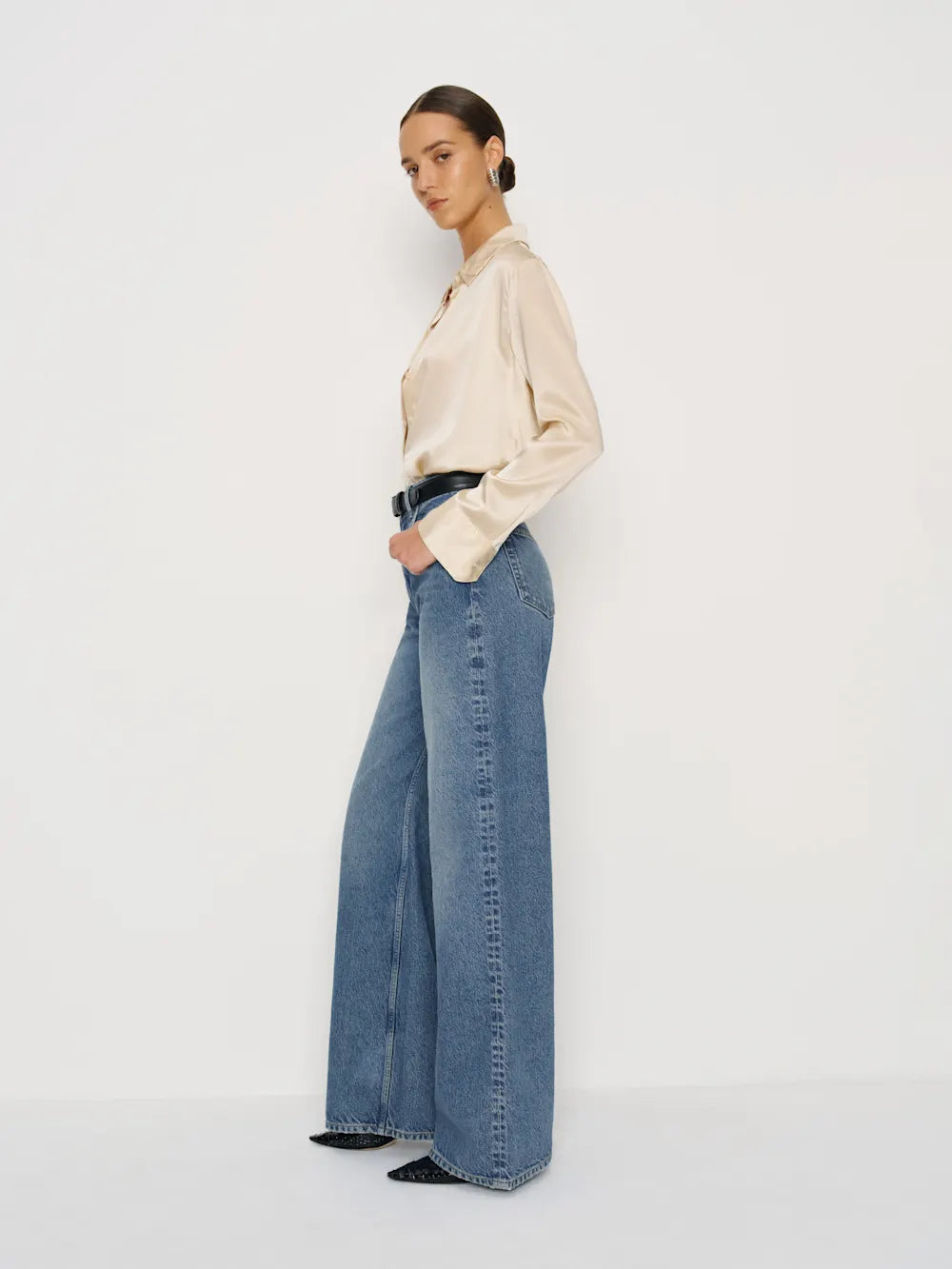 Person wearing a beige blouse and blue jeans on a white background