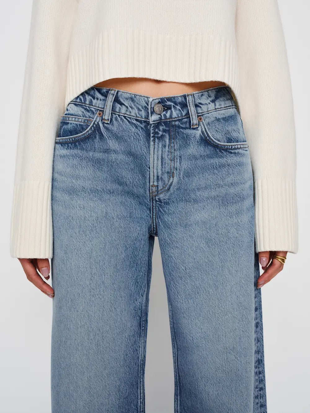 Light blue jeans worn with a white sweater on a plain background