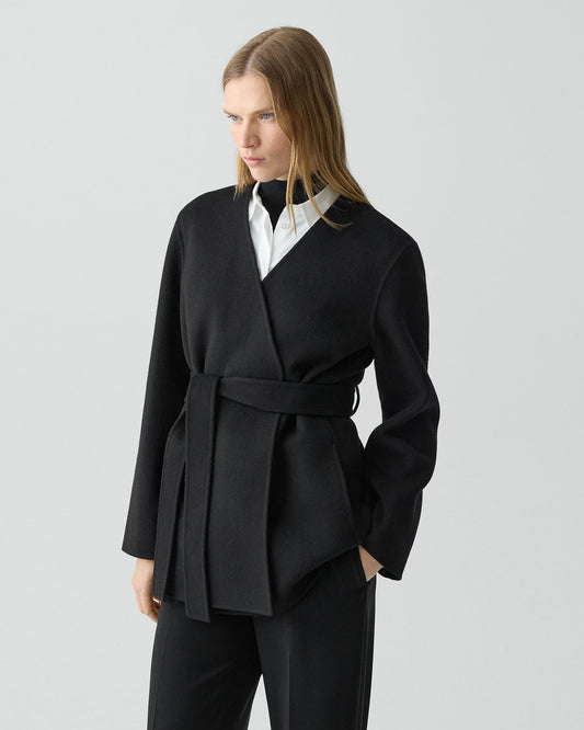 Woman wearing a black coat with a white shirt on a light gray background
