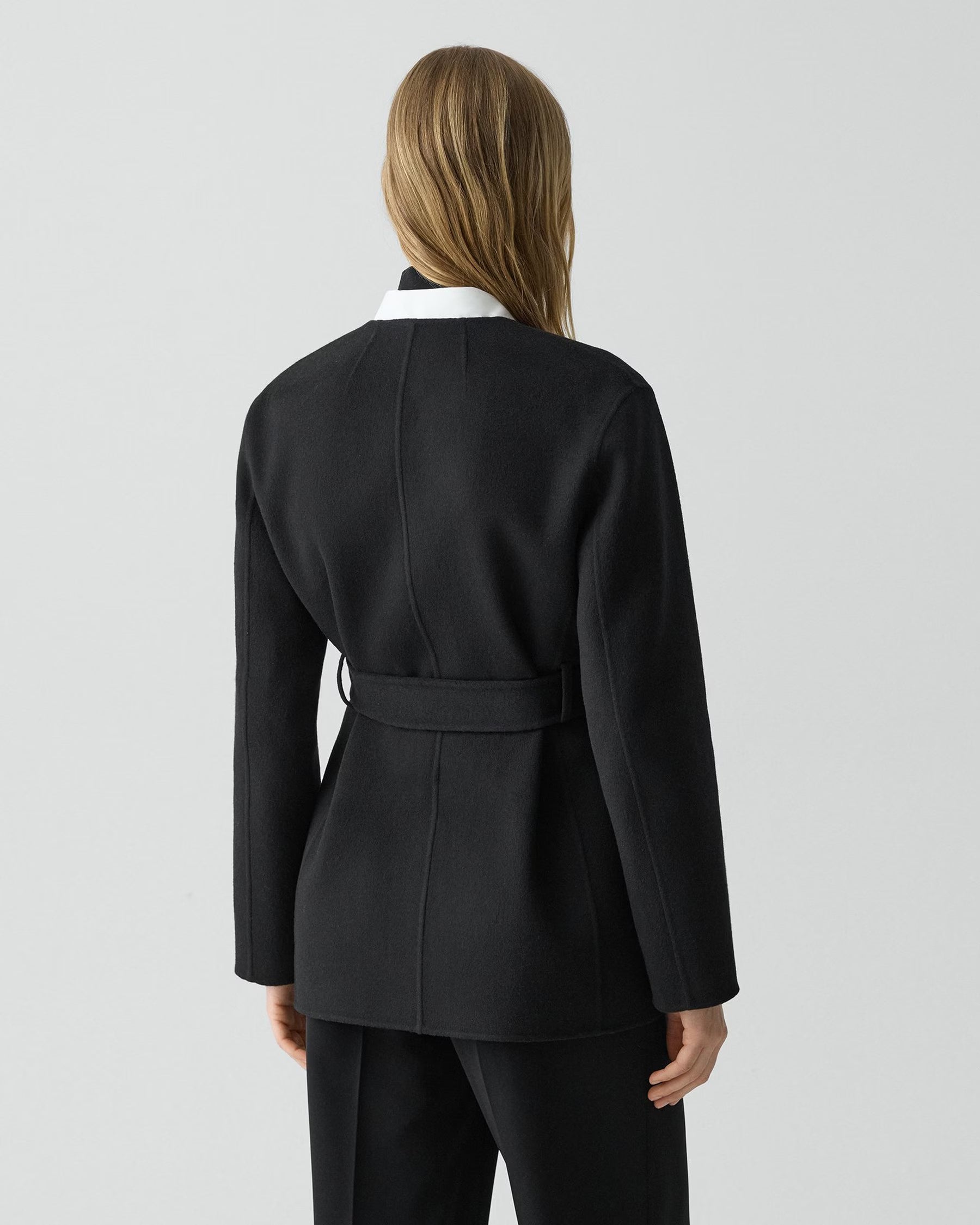 Person wearing a black coat with a white collar on a light gray background
