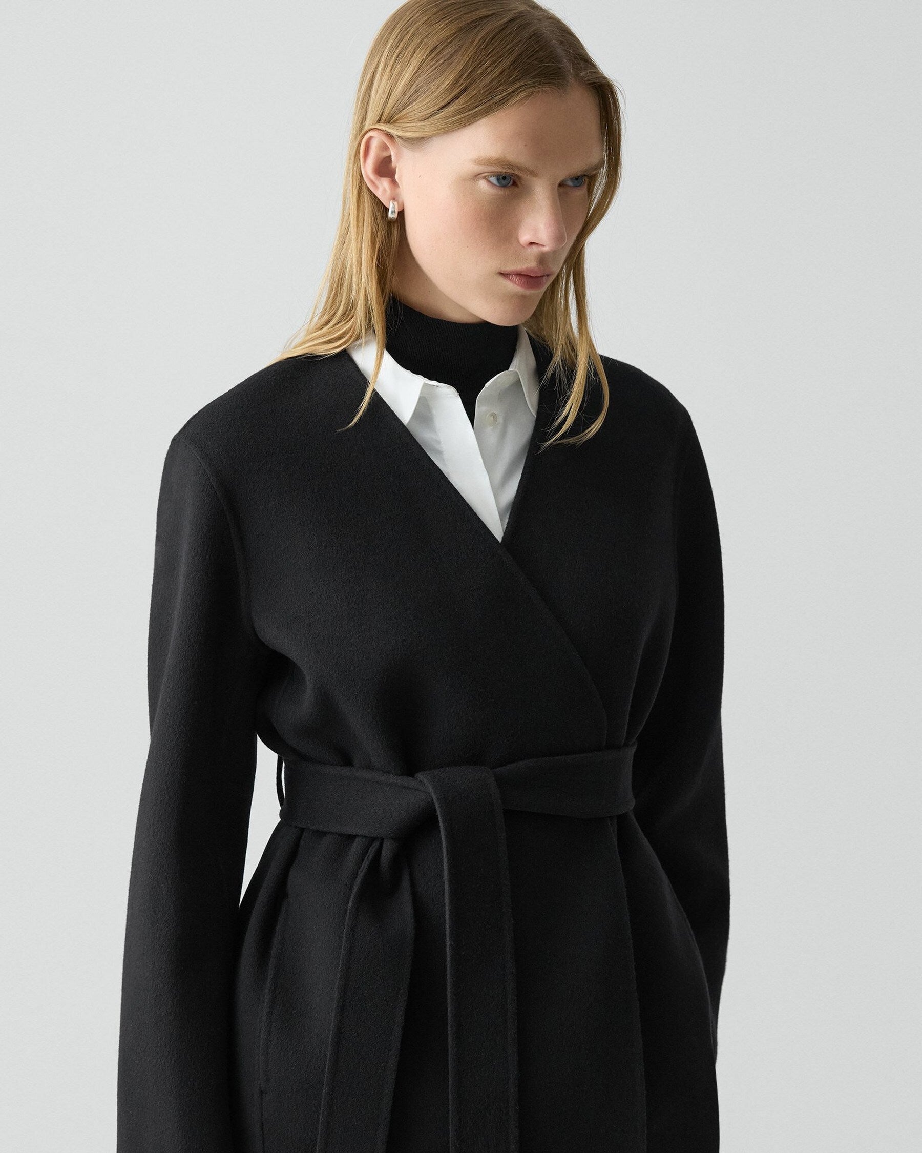 Woman wearing a black coat over a white shirt on a light gray background