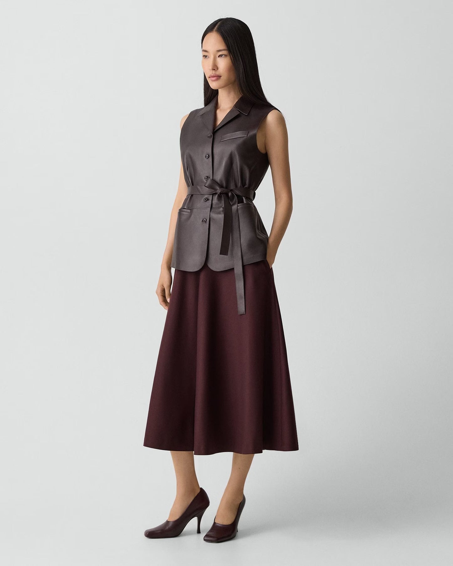 Woman wearing a sleeveless brown top and skirt set on a light gray background