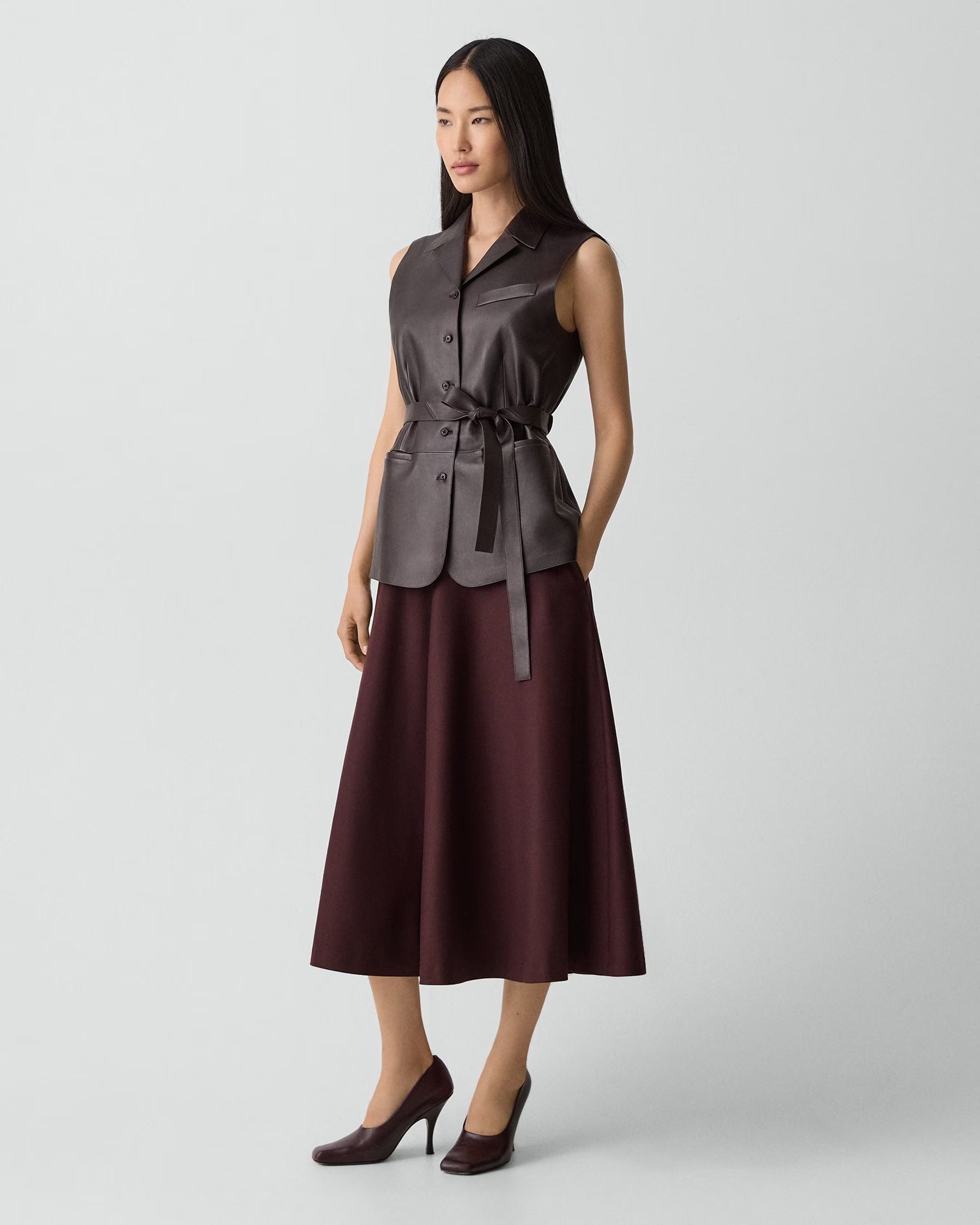Woman wearing a sleeveless brown top and skirt set on a light gray background
