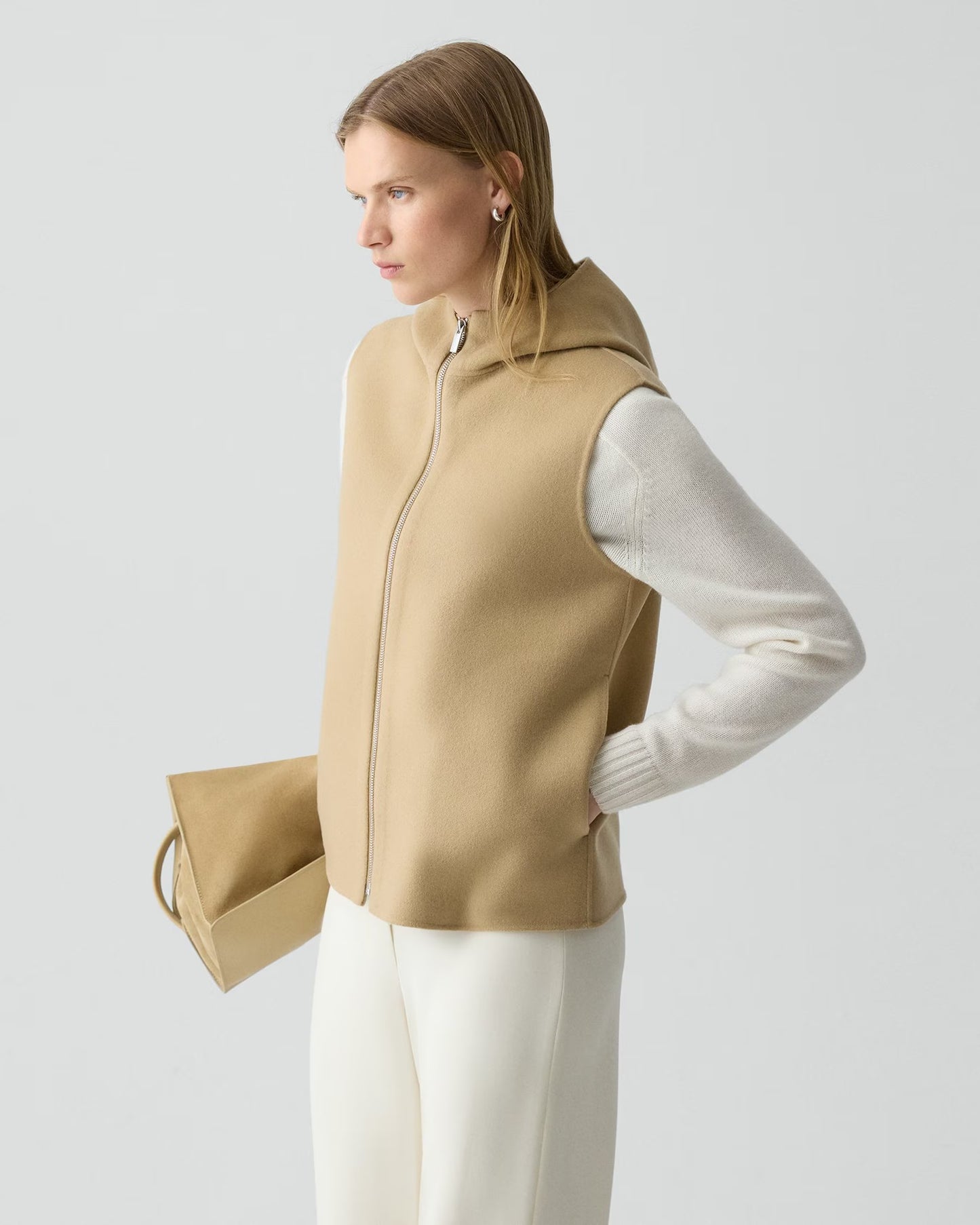 Woman wearing a beige vest over a white long-sleeve shirt on a light gray background