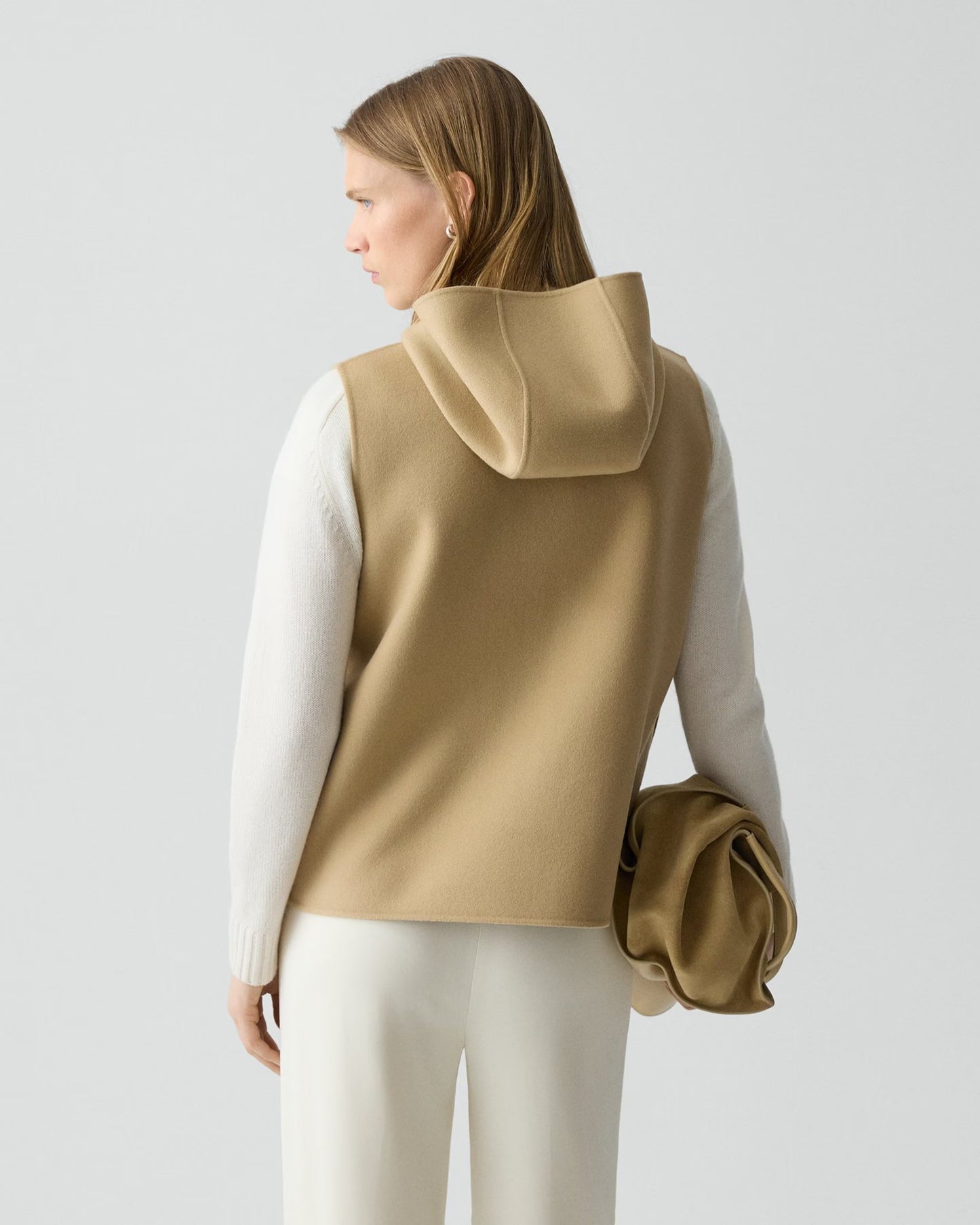 Woman wearing a beige hooded vest over a white long-sleeve shirt on a light gray background