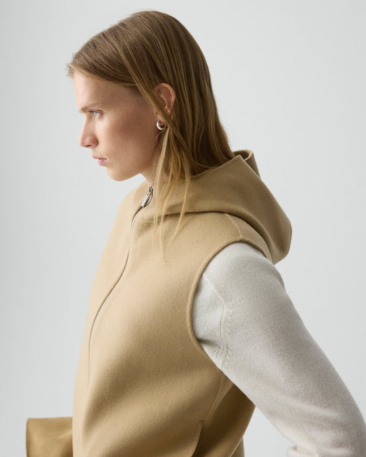 Woman wearing a beige vest over a white shirt on a light gray background