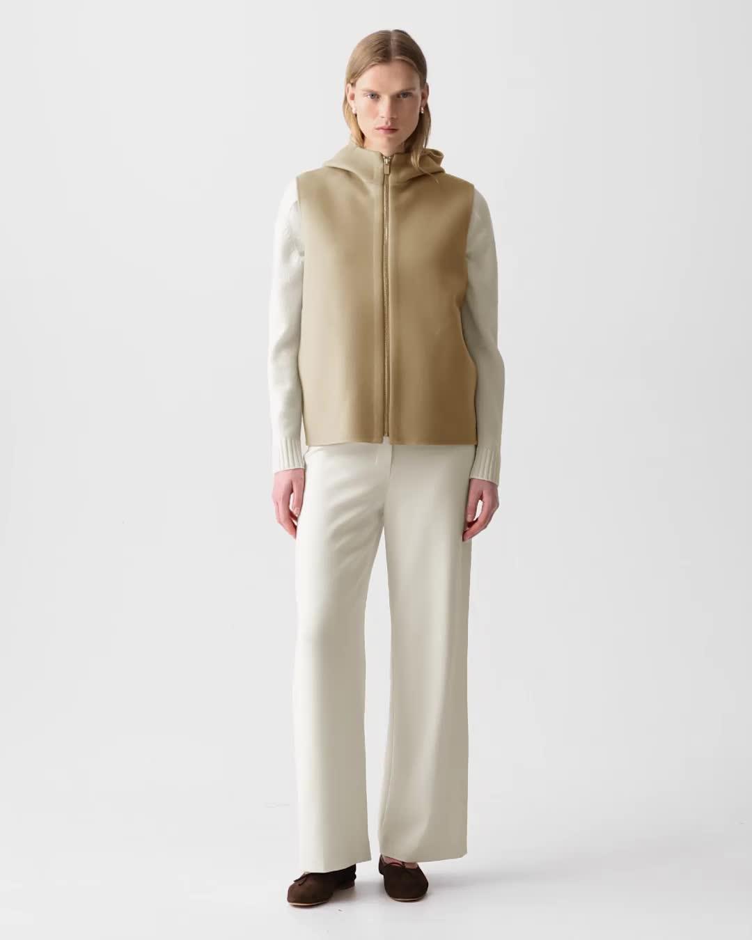 Person wearing a beige vest over a white shirt with beige pants on a white background