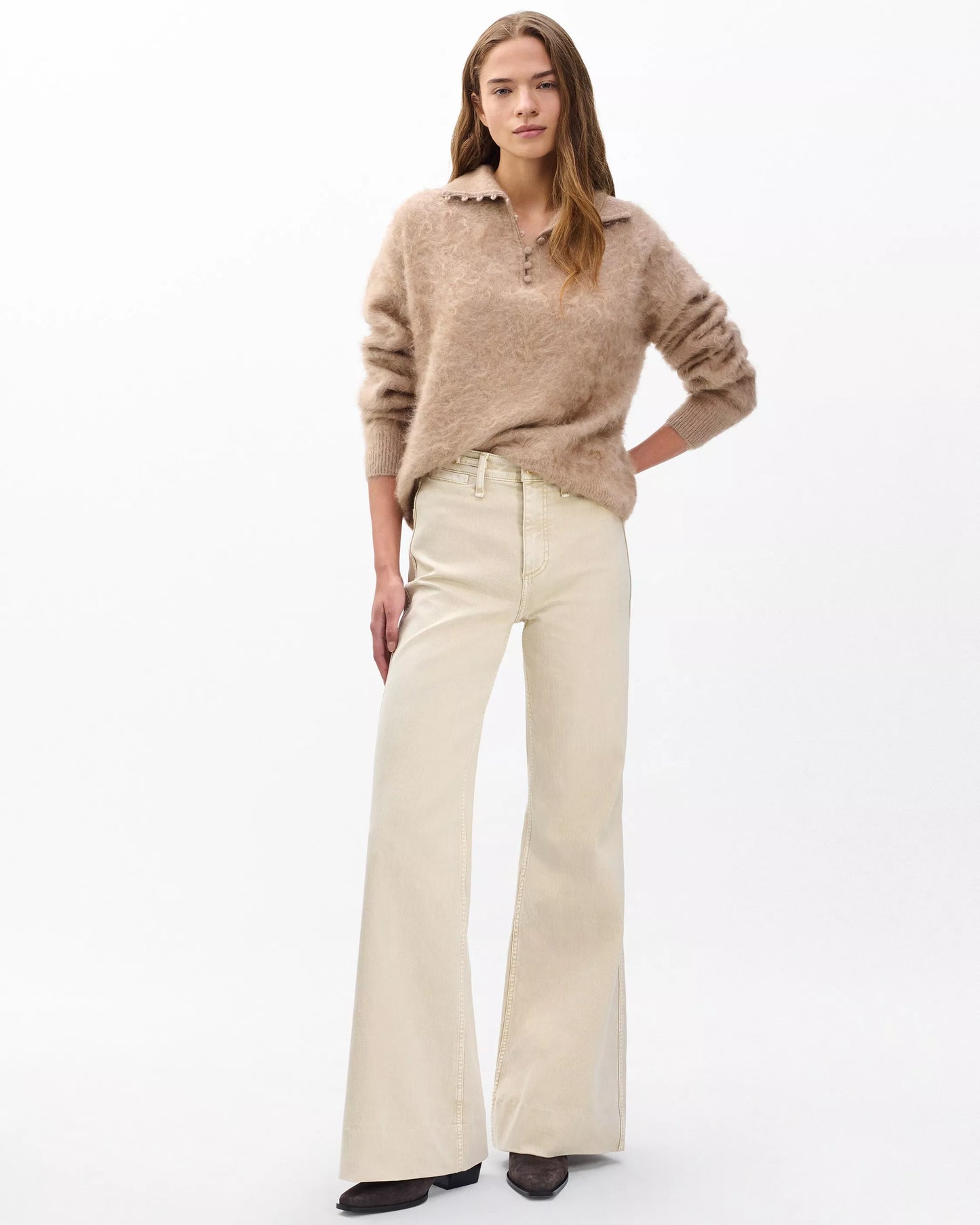 Woman wearing a beige sweater and white pants on a white background