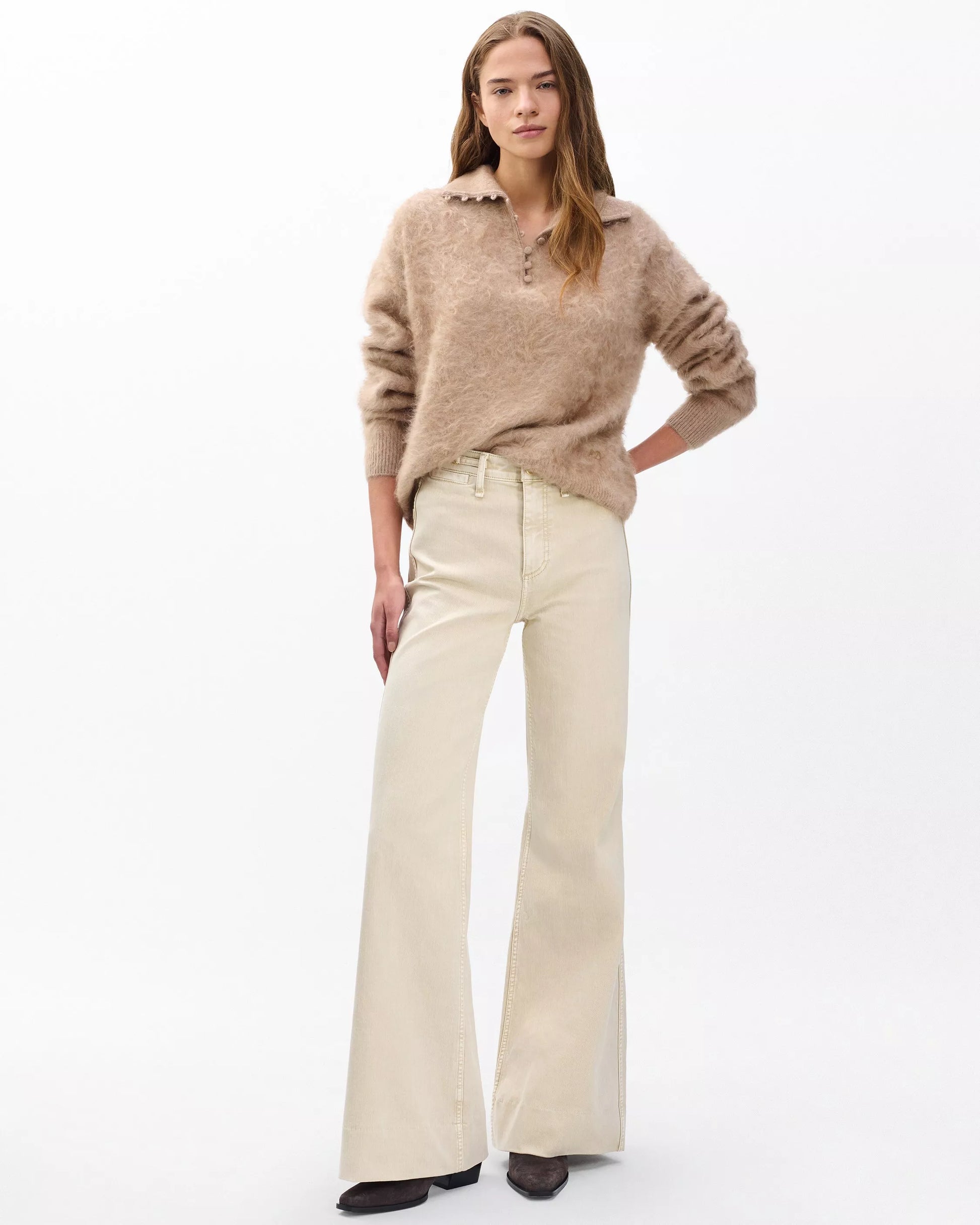 Woman wearing a beige sweater and white pants on a white background