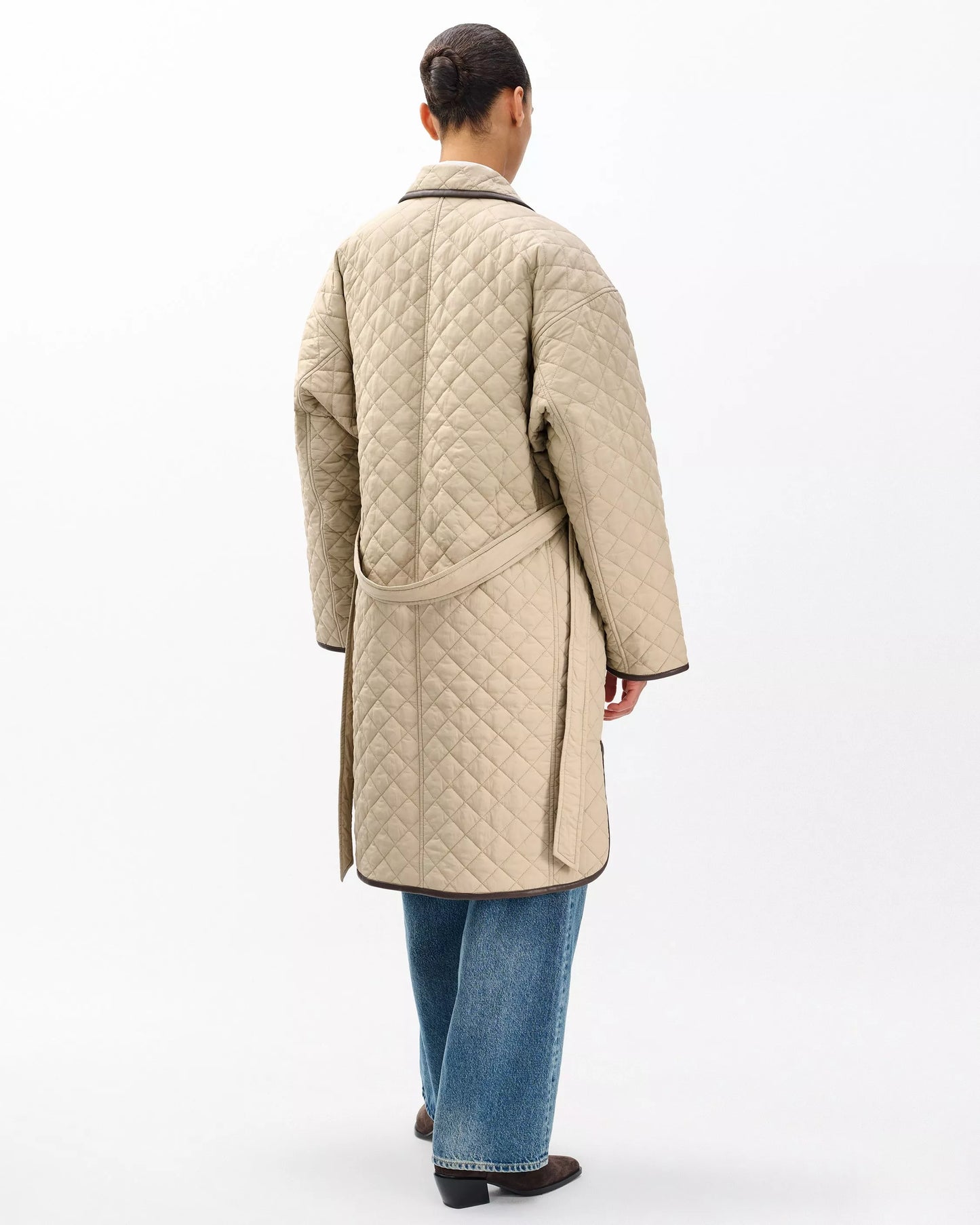 Person wearing a beige quilted coat on a white background