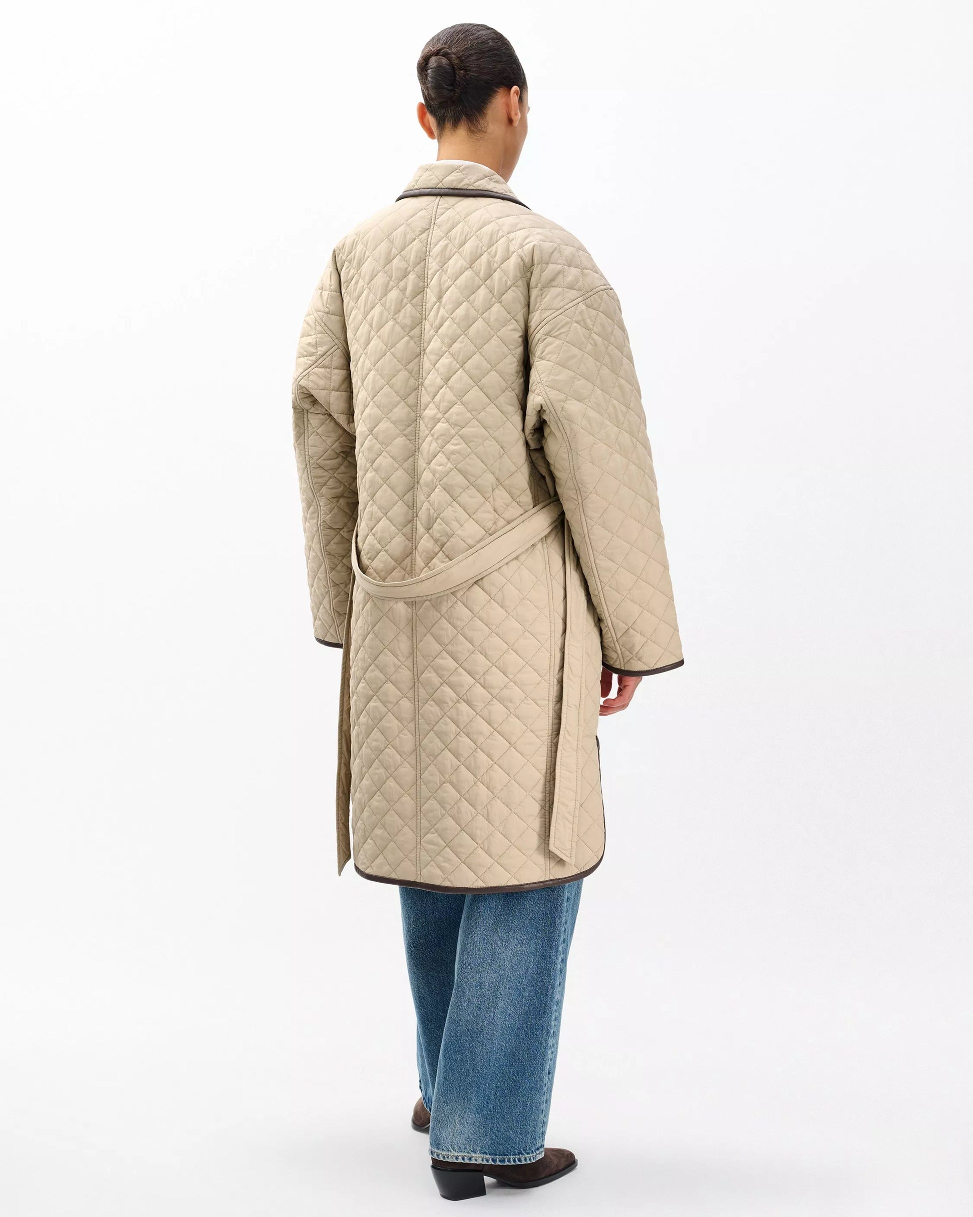 Person wearing a beige quilted coat on a white background
