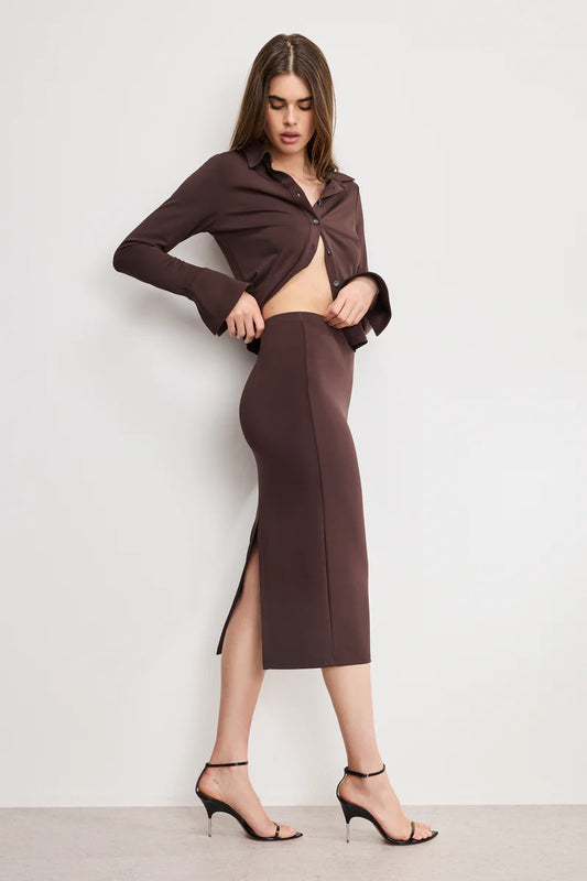 Woman wearing a brown outfit with a slit skirt against a white background