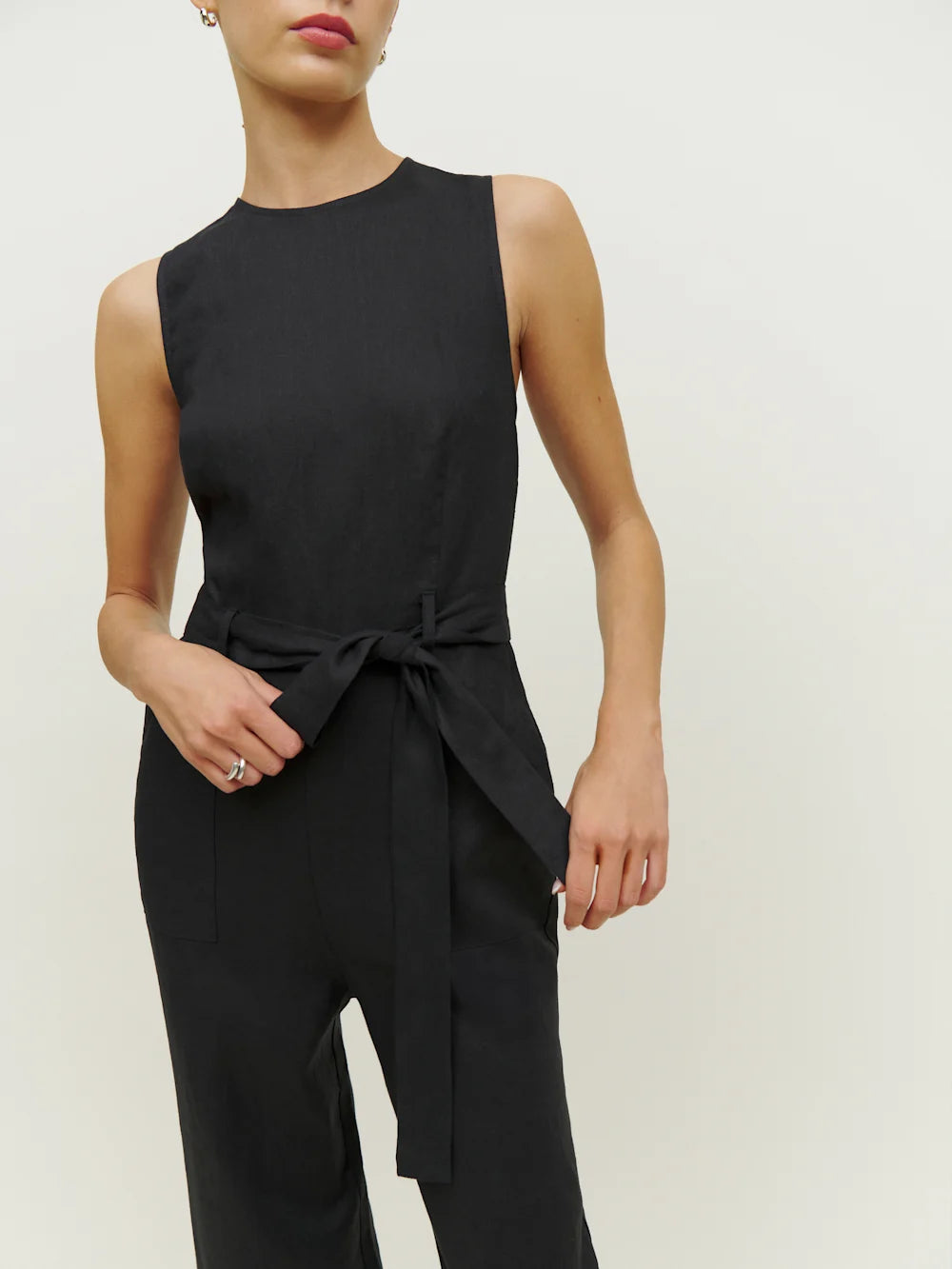 Person wearing a black sleeveless jumpsuit with a tie waist on a plain background