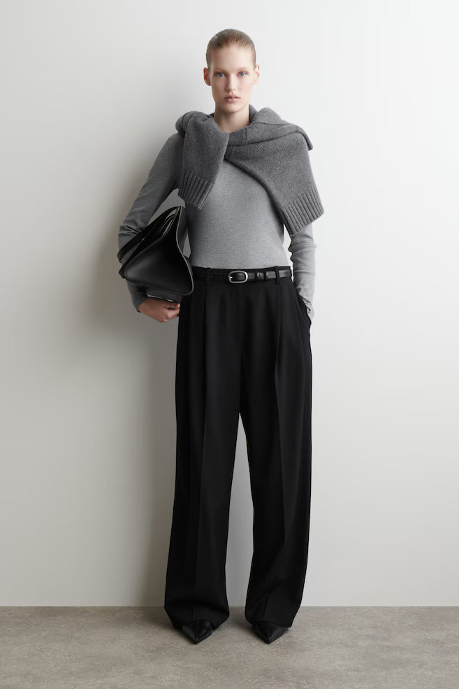 Person wearing a gray sweater and black pants against a plain background