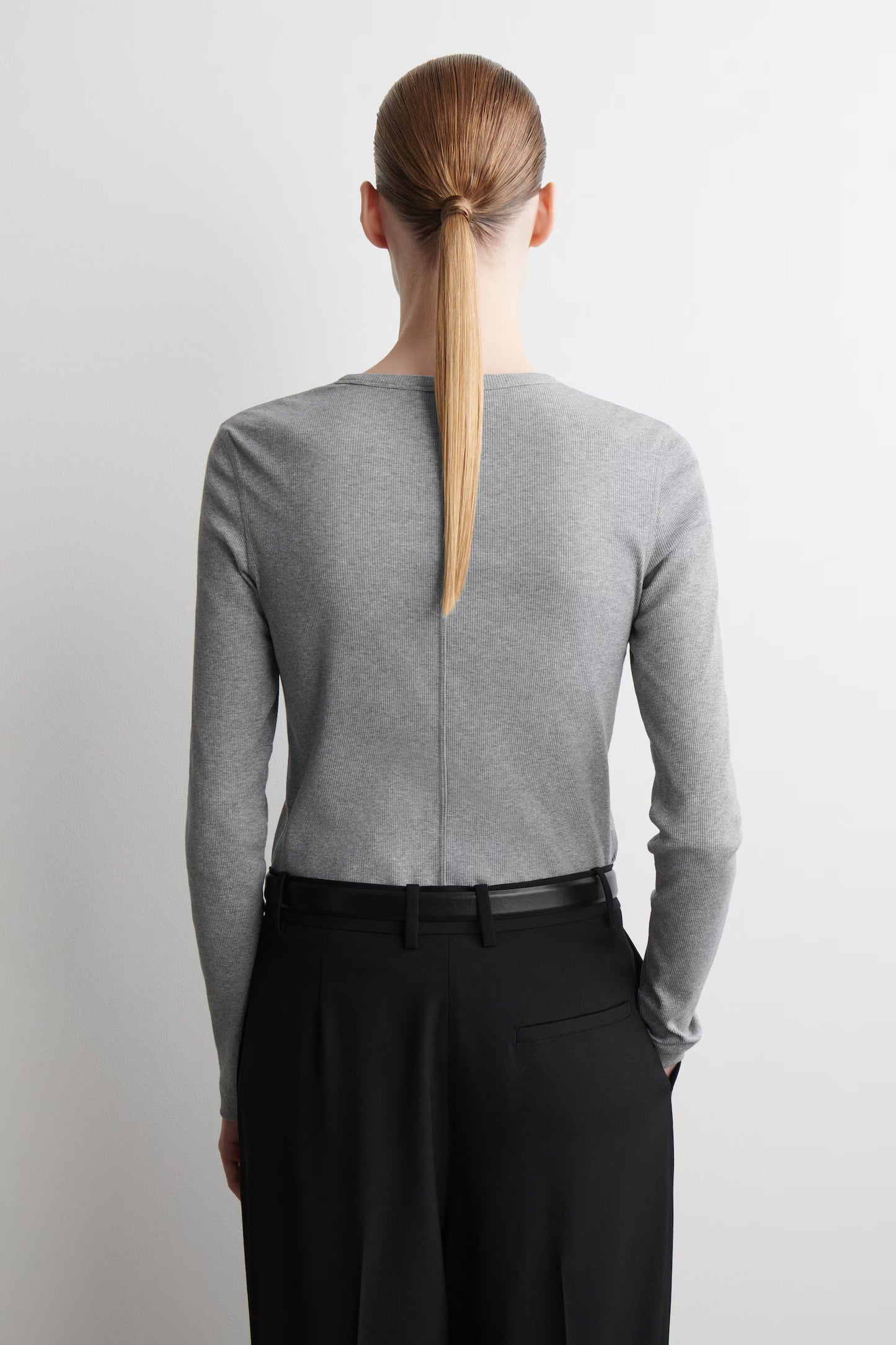 Person wearing a gray sweater and black pants with a plain background