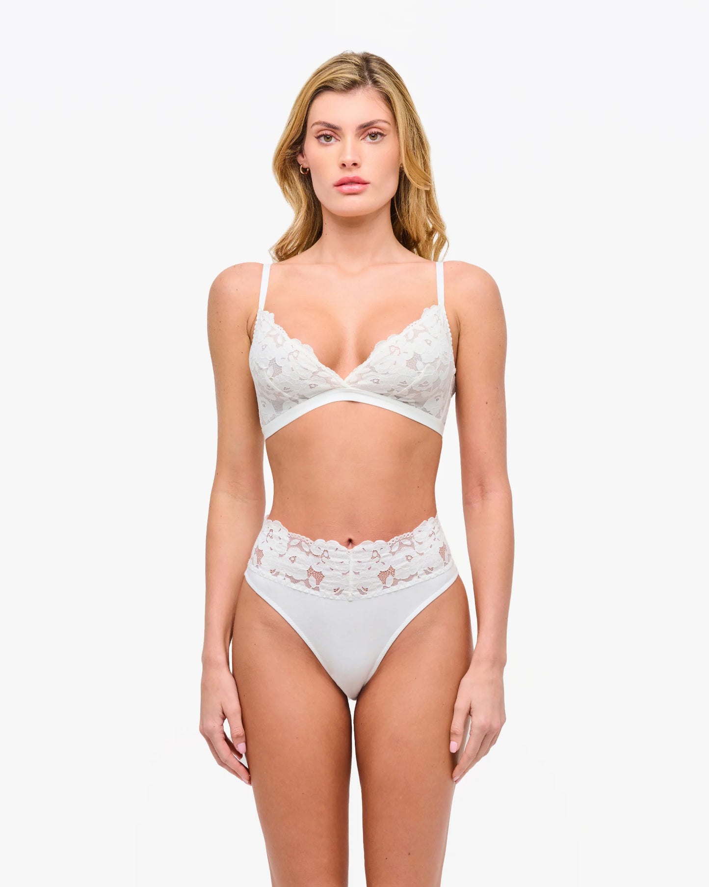 Woman wearing a white lace lingerie set on a plain background
