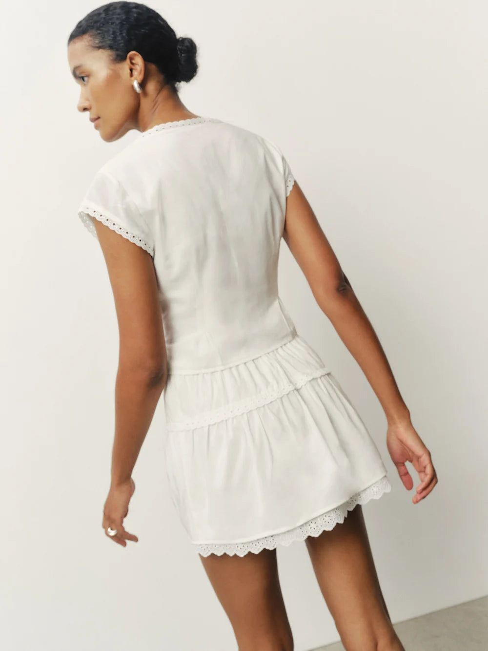Woman wearing a white lace-trimmed dress against a plain background