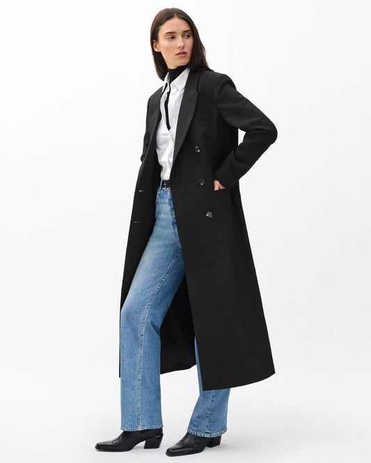 Person wearing a long black coat, white shirt, blue jeans, and black shoes on a white background
