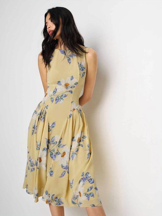 Anelis Dress in black viscose georgette, showcasing its boat neckline and fluid A-line silhouette on a woman in a garden setting