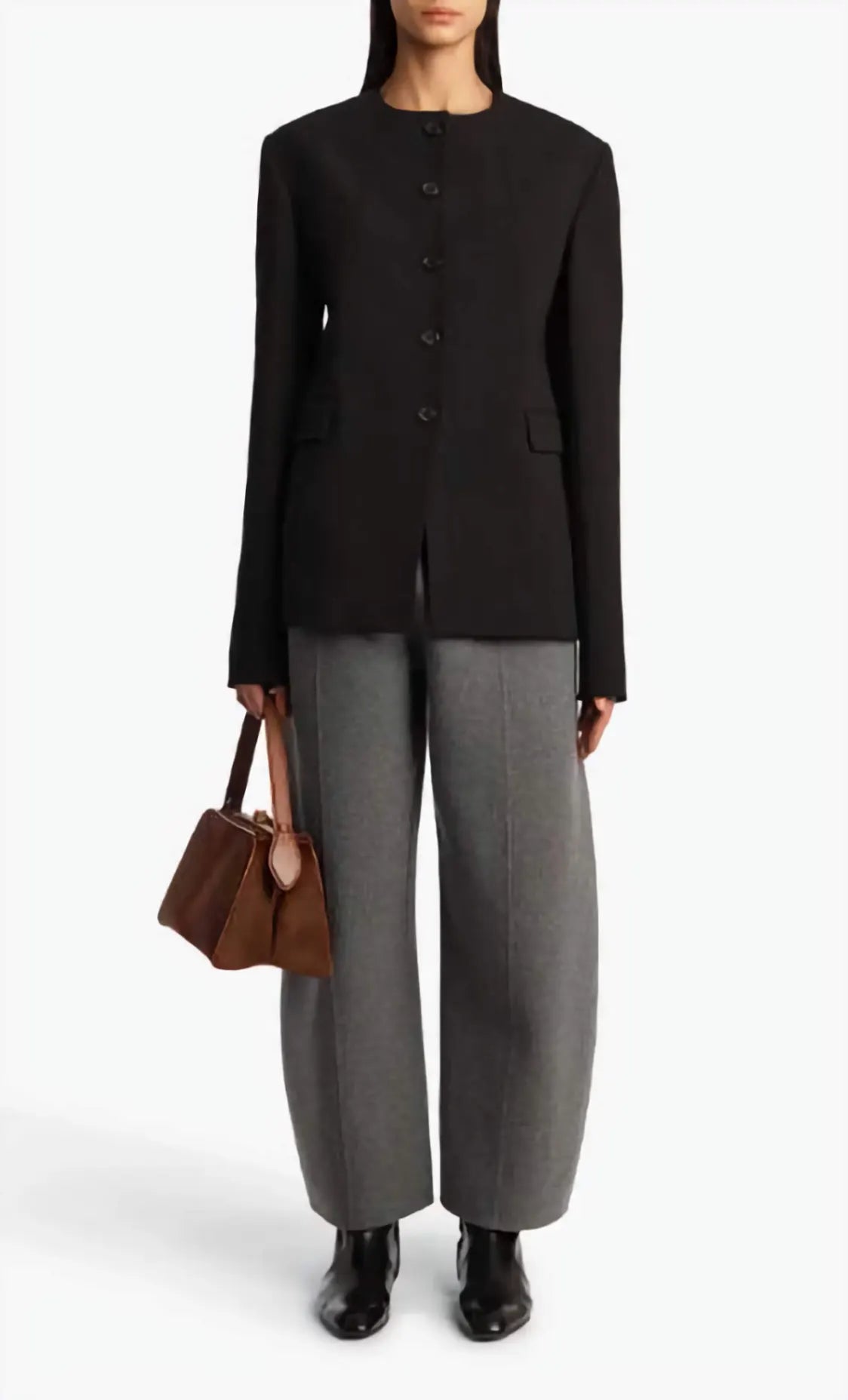 Person wearing a black jacket, gray pants, and holding a brown handbag on a white background