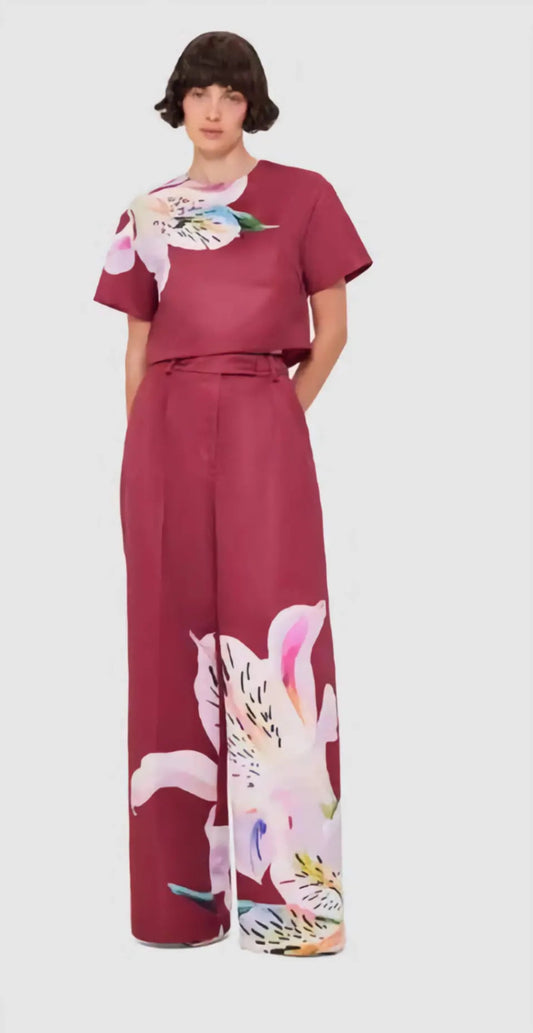 The Elisha Wide Leg Pants in deep burgundy with an oversized lily print, shown on a model in motion, highlighting the fluid silhouette and high-rise waist