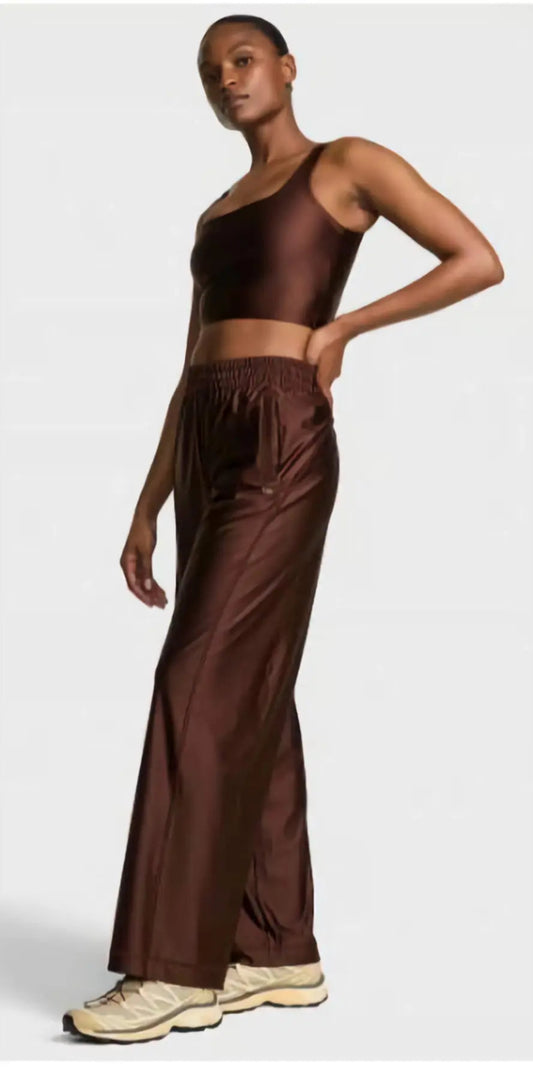 VSX GlossyTech Wide-Leg Pant in black, showcasing its high-shine finish and fluid, wide-leg silhouette on a woman in motion
