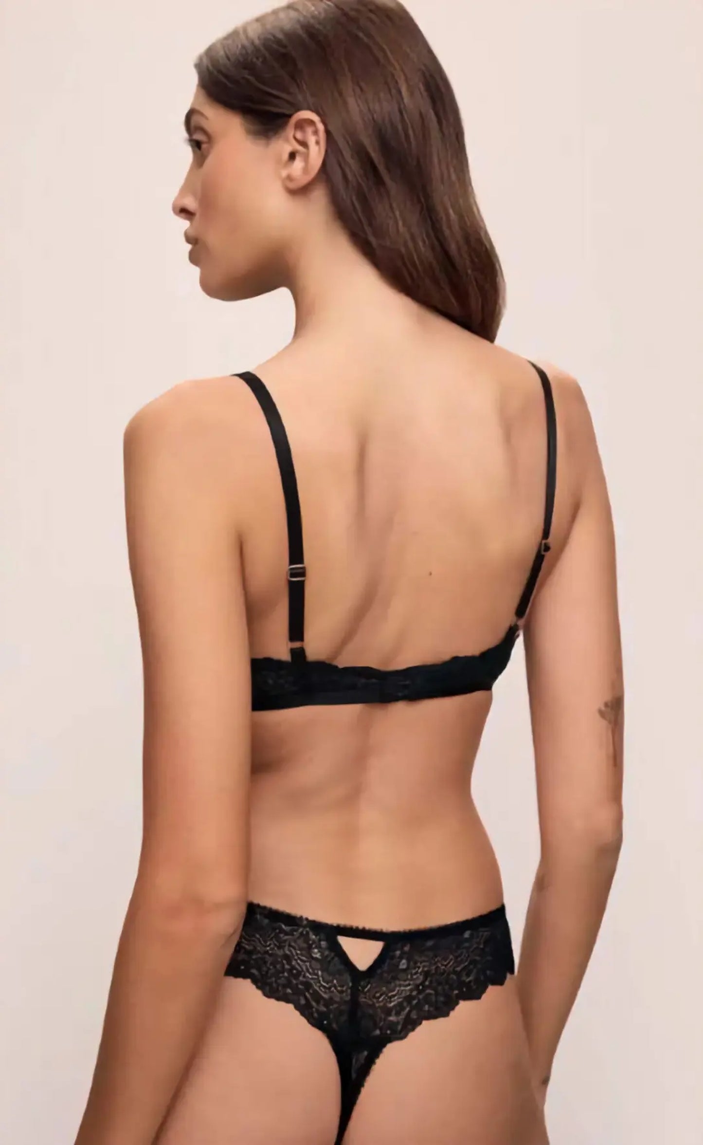 Woman wearing a black lace bra and panties set on a beige background