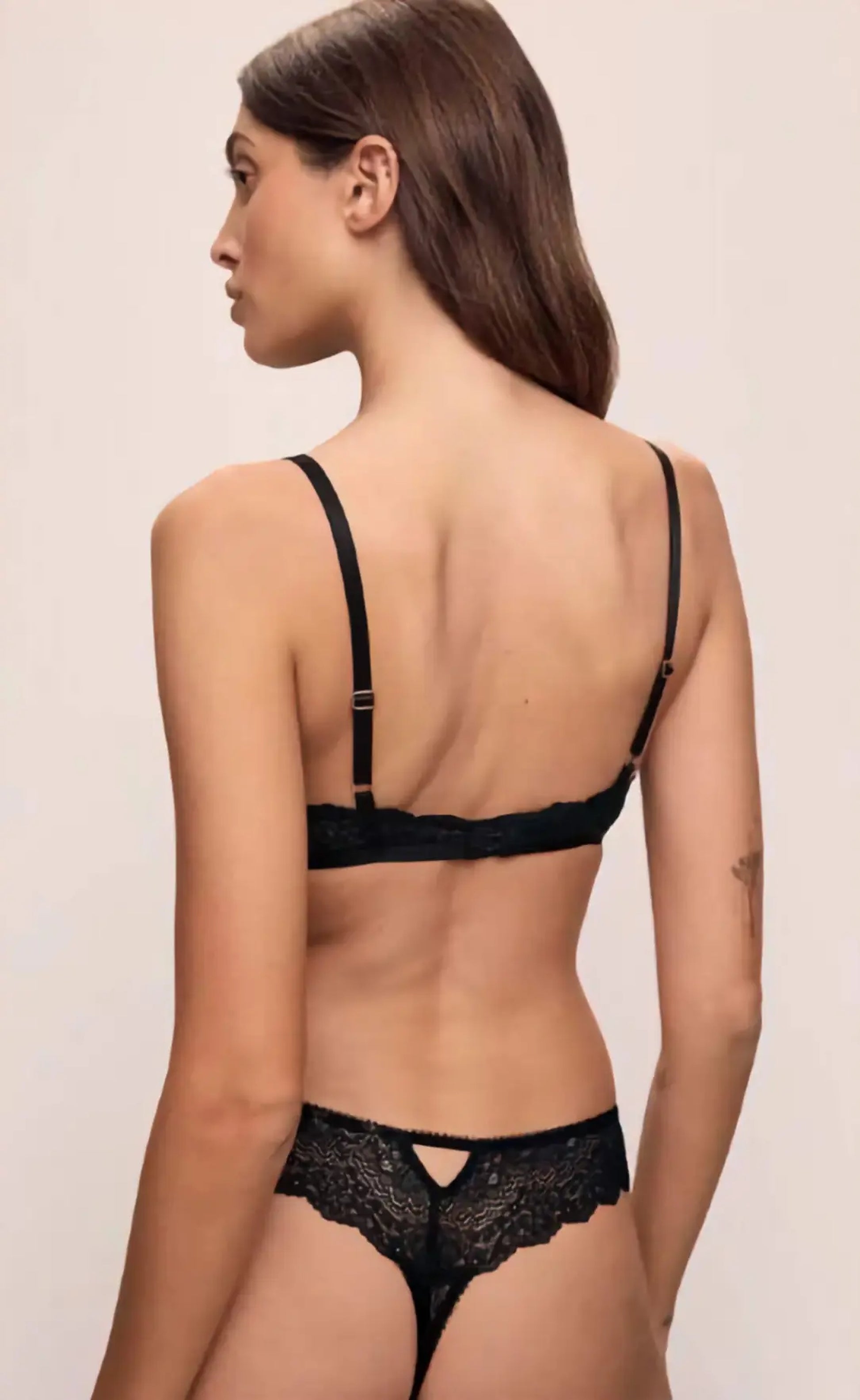 Woman wearing a black lace bra and panties set on a beige background