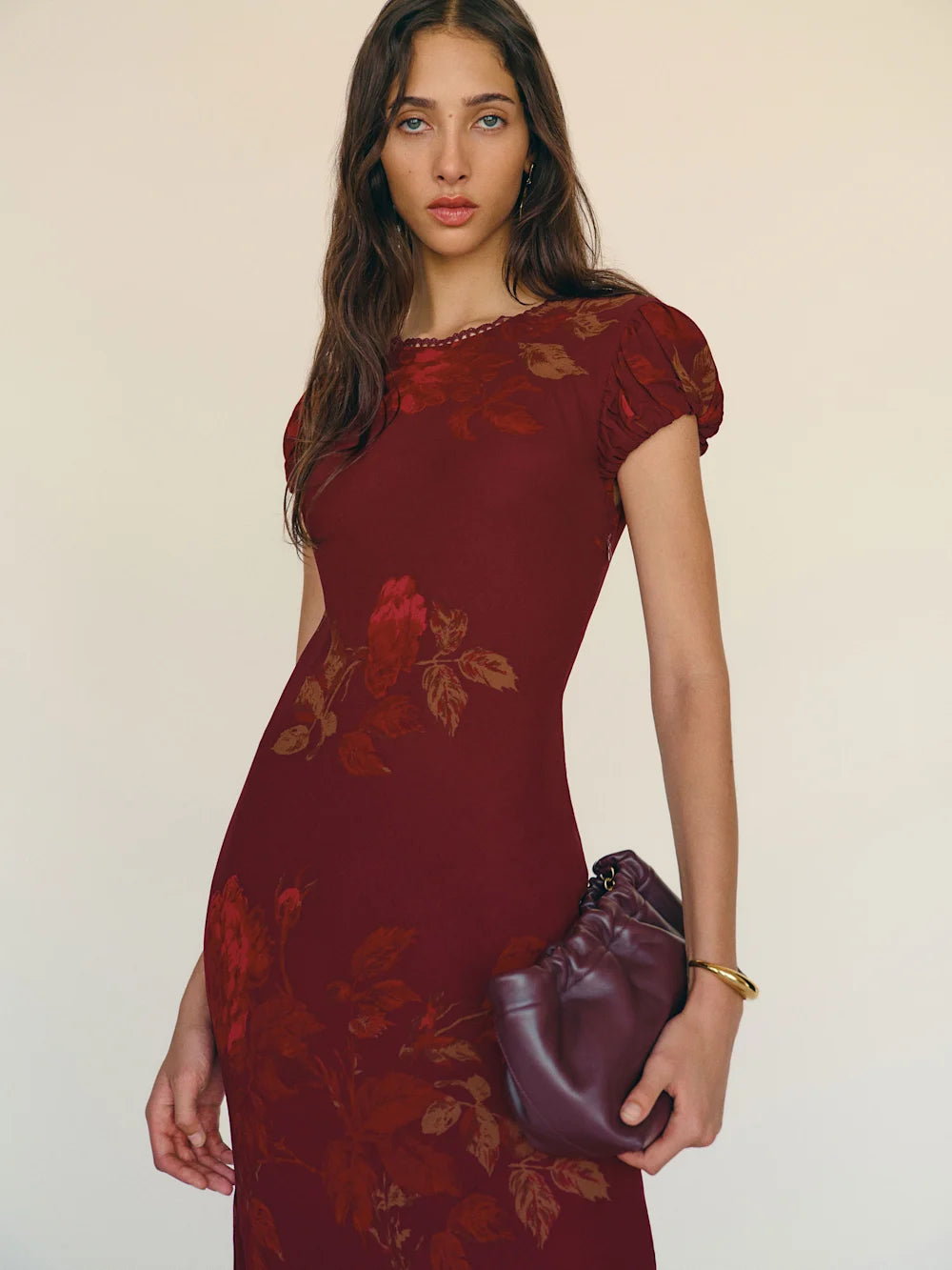 Woman wearing a burgundy dress with floral patterns against a plain background