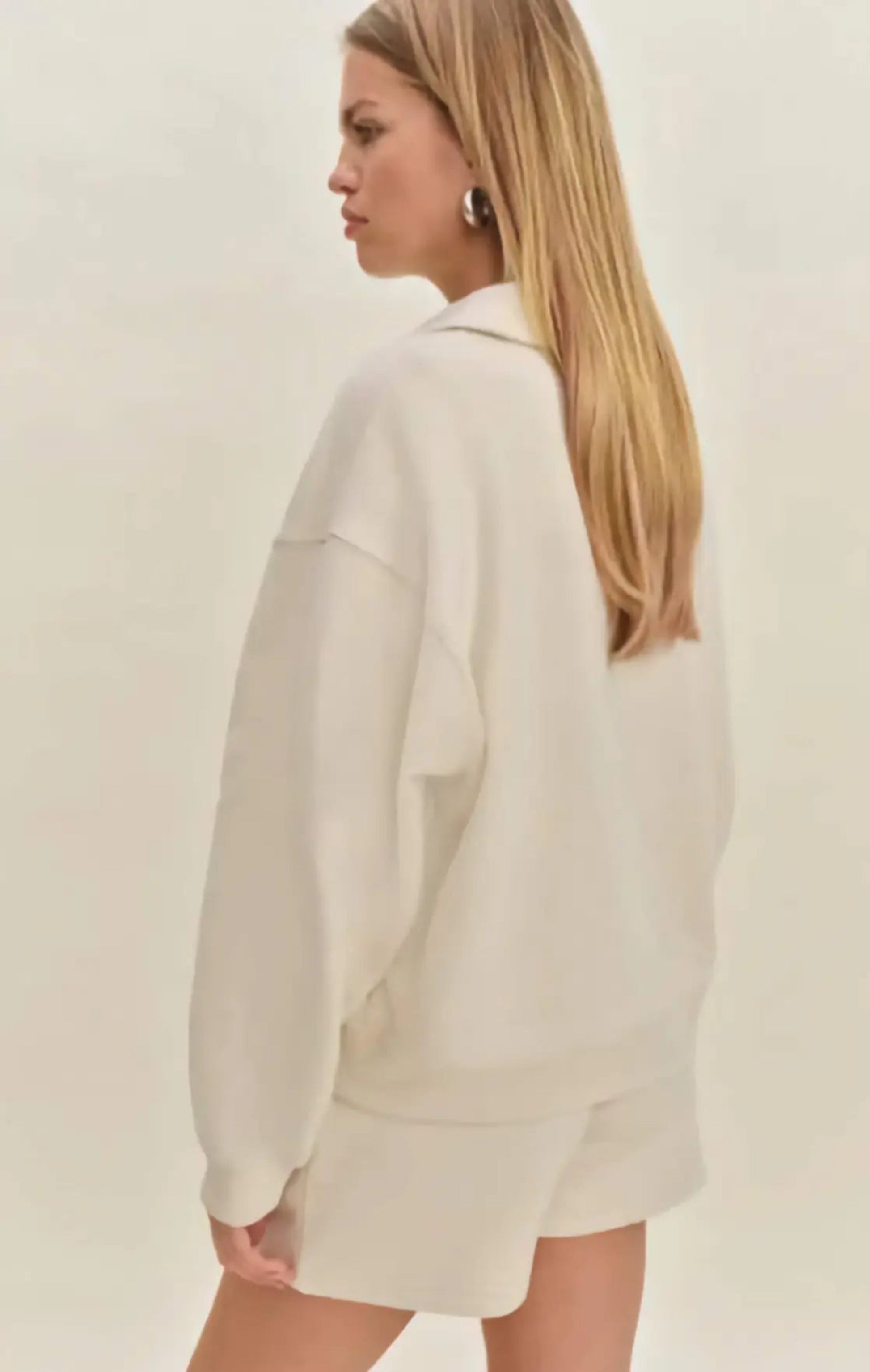 Woman in a modern setting wearing the Nico Classic Polo Sweatshirt in cream, embodying elevated comfort and strategic recalibration.