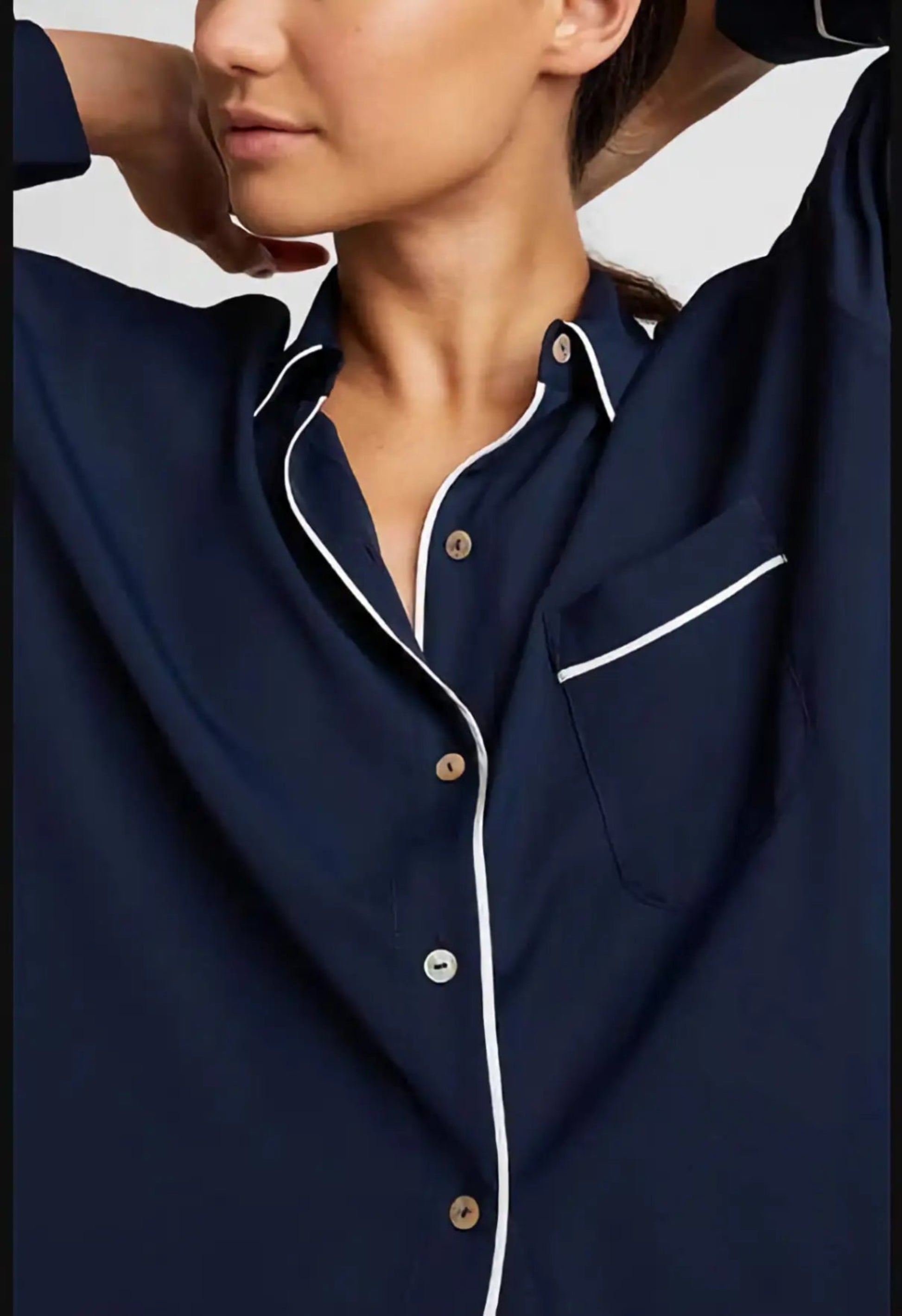 Navy blue pajama top with white trim worn by a person, on a plain background