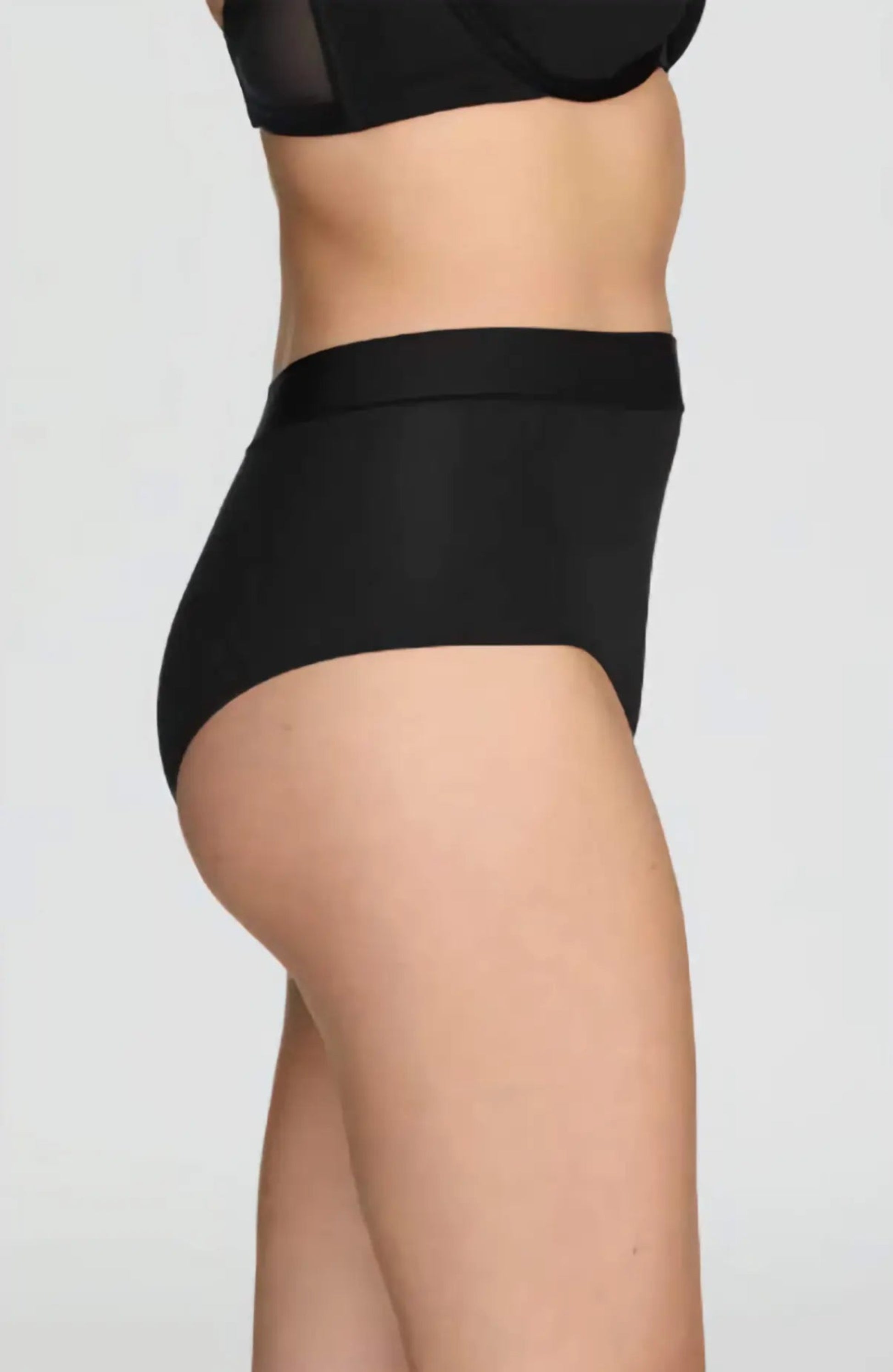 Person wearing black high-waisted underwear on a plain background